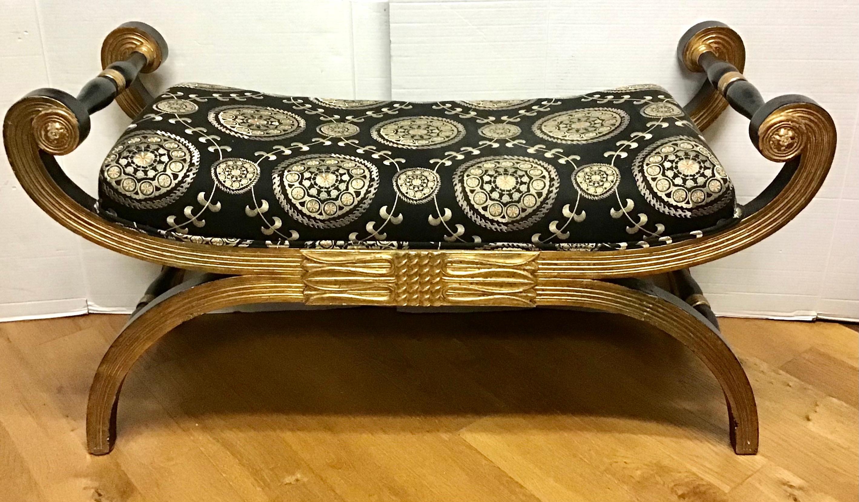 Well carved giltwood Regency style bench with scroll arms supported by a stretcher base frame with a custom upholstered seat with black and gold fabric.