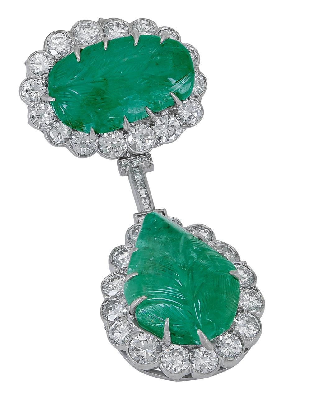 A unique diamond brooch that features two carved green emeralds each surrounded by a row of round brilliant diamonds. The emerald and diamond halo is attached by a thin yet durable wire accented with diamonds. 
Emeralds weigh 68 carats