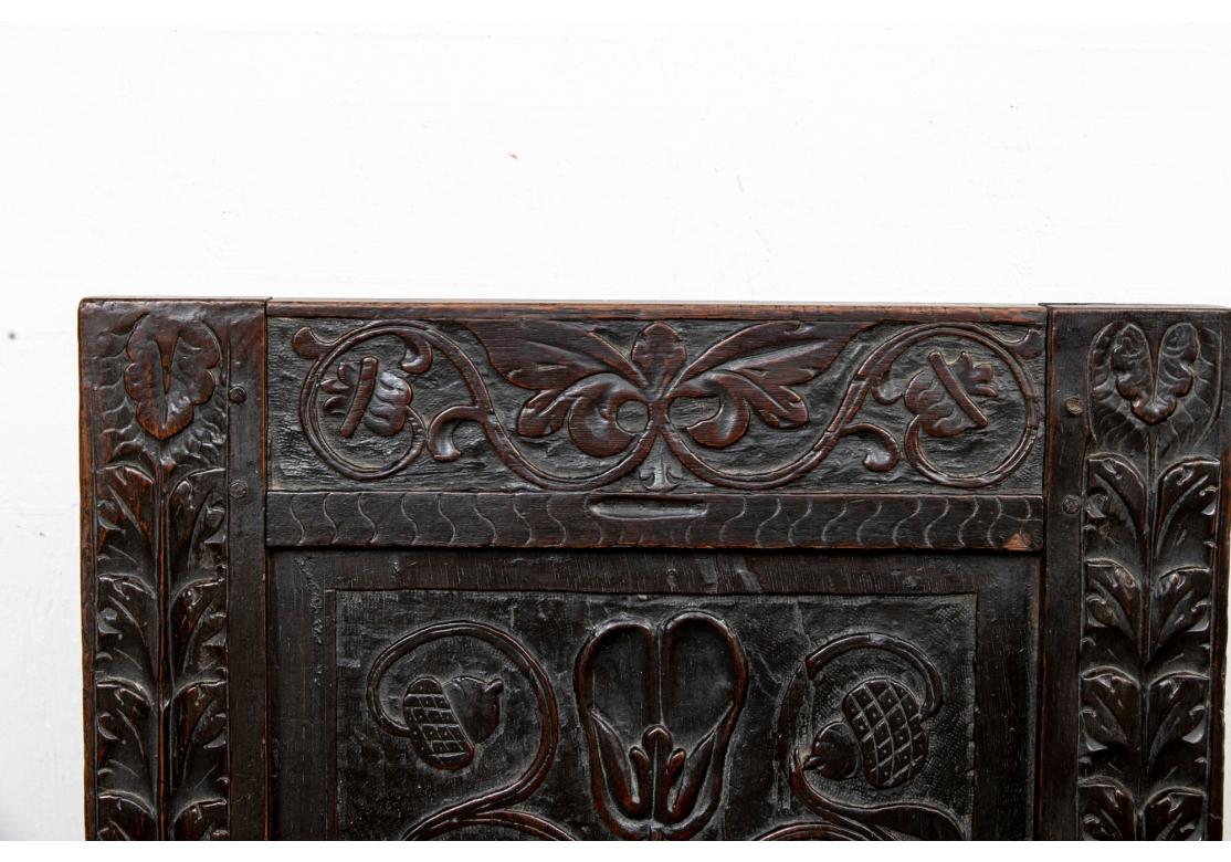 A particularly fine Carved Armchair in a Jacobean related style. In a very dark stain with a tall back and relief carved decoration of an urn with floral vines and separate carved sides with tall stemmed leafy flowers. The crest rail with a foliate