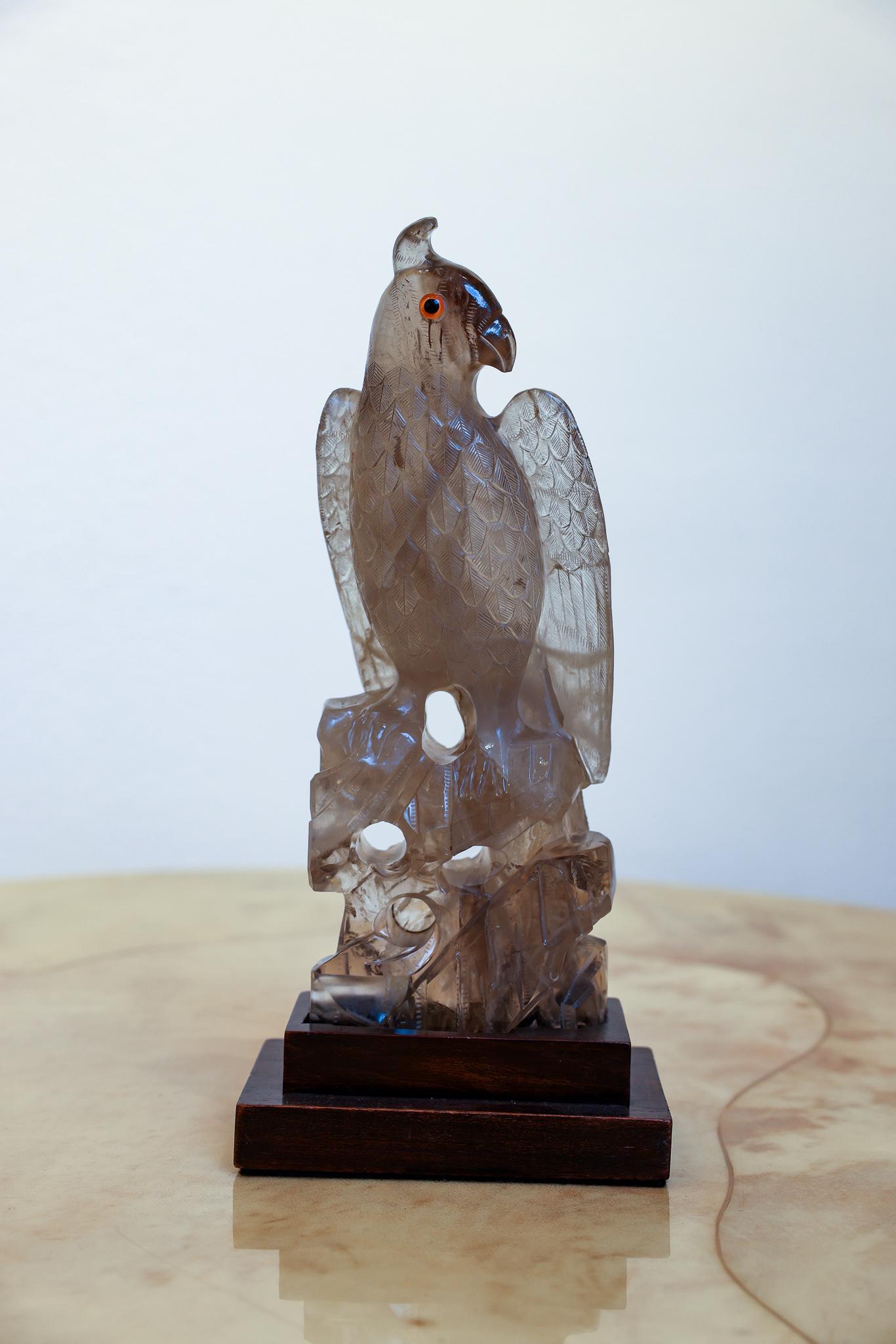 This majestic eagle is hand carved from quality smoky quartz. The eagle is standing on a decorative geometric base that has been custom made for this purpose. With faux glass eyes, the eagle is looking over his left wing. The detail, particularly in