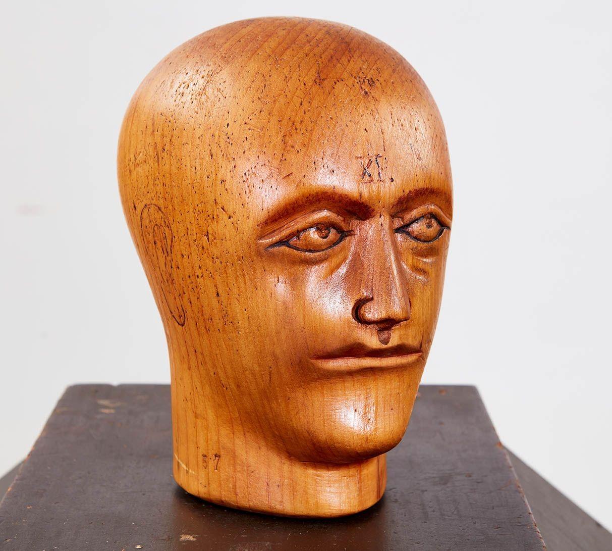 A wooden mannequin head, probably a toupe stand, with good color and a well-carved idiosyncratic and compelling face, having laconic eyes and with what might be chewing tobacco in his upper right lip.  Roman numerals XI stamped above the bridge of