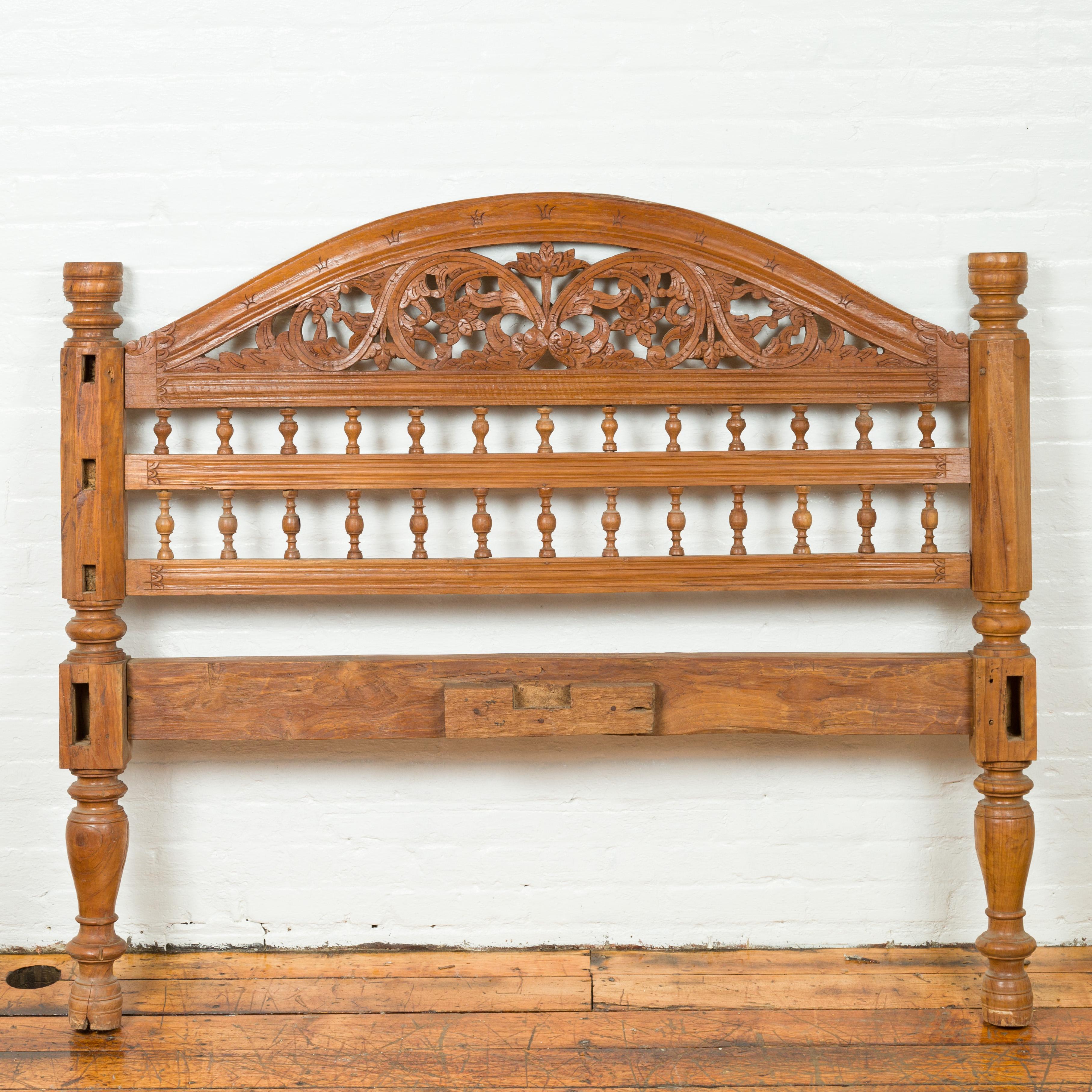 A carved vintage Indonesian headboard from the mid-20th century, with scrolling foliage and petite balusters. Crafted in Indonesia, this carved wooden headboard features a bonnet-shaped upper rail, resting upon delicately carved scrolling foliage.