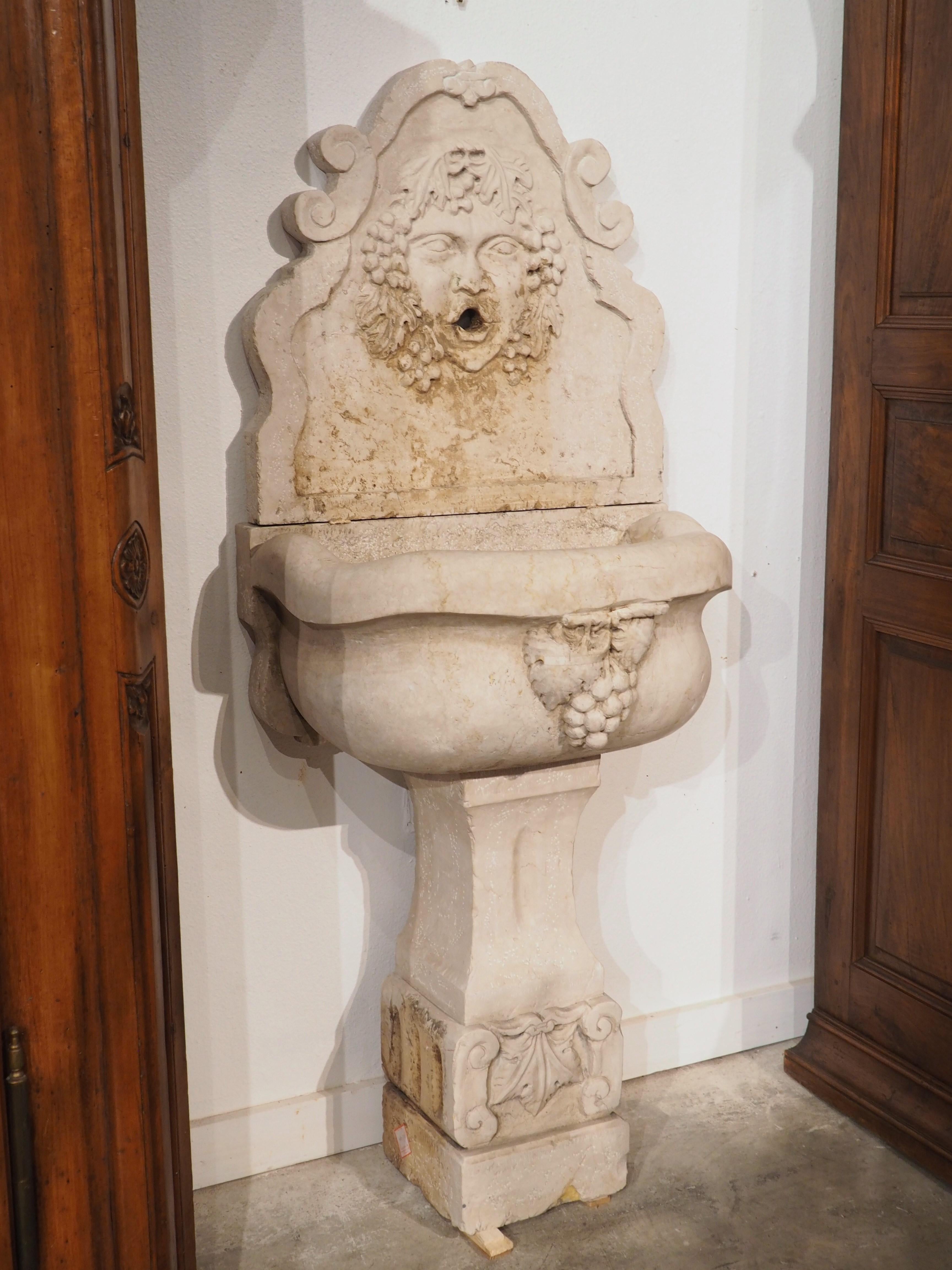 Comprised of three pieces of hand-carved Italian marble, this wall fountain features a neoclassical depiction of the Roman god Bacchus (his Greek name was Dionysus). As Bacchus was the god of winemaking, he is often depicted in art with symbolic