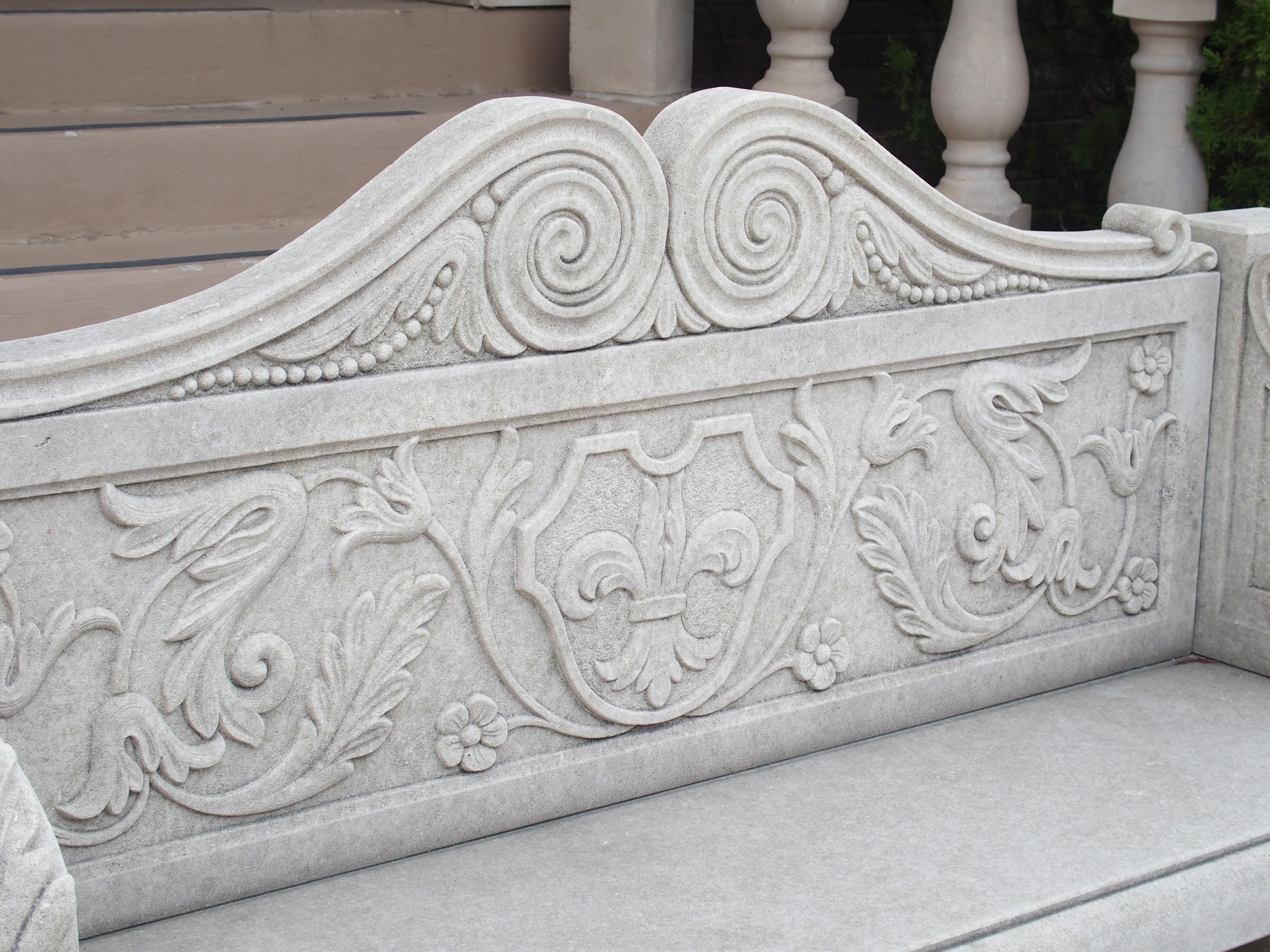 Hand-carved in Italy, this limestone garden bench features elaborate foliate motifs, including a fleur de lys and acanthus leaves. Consisting of six carved pieces of stone, the beautiful bench has developed a phenomenal dark gray patina over the