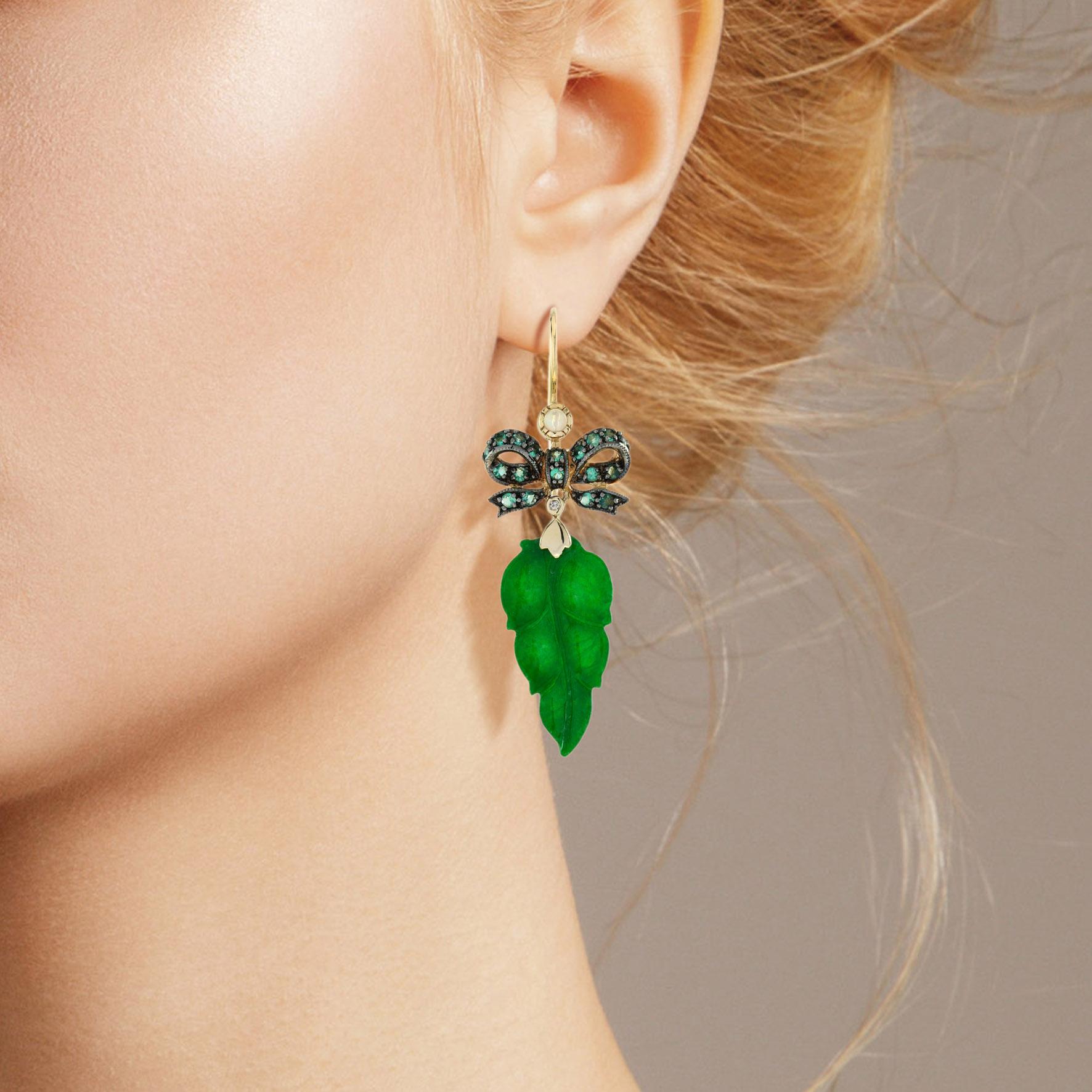 The natural jade in these lovely earrings has some very special shape. Both pieces have a strong green color and well leaf carvings. The jade is suspended in a 9k yellow gold setting with emerald ribbon bow on the top. The earrings transfer their