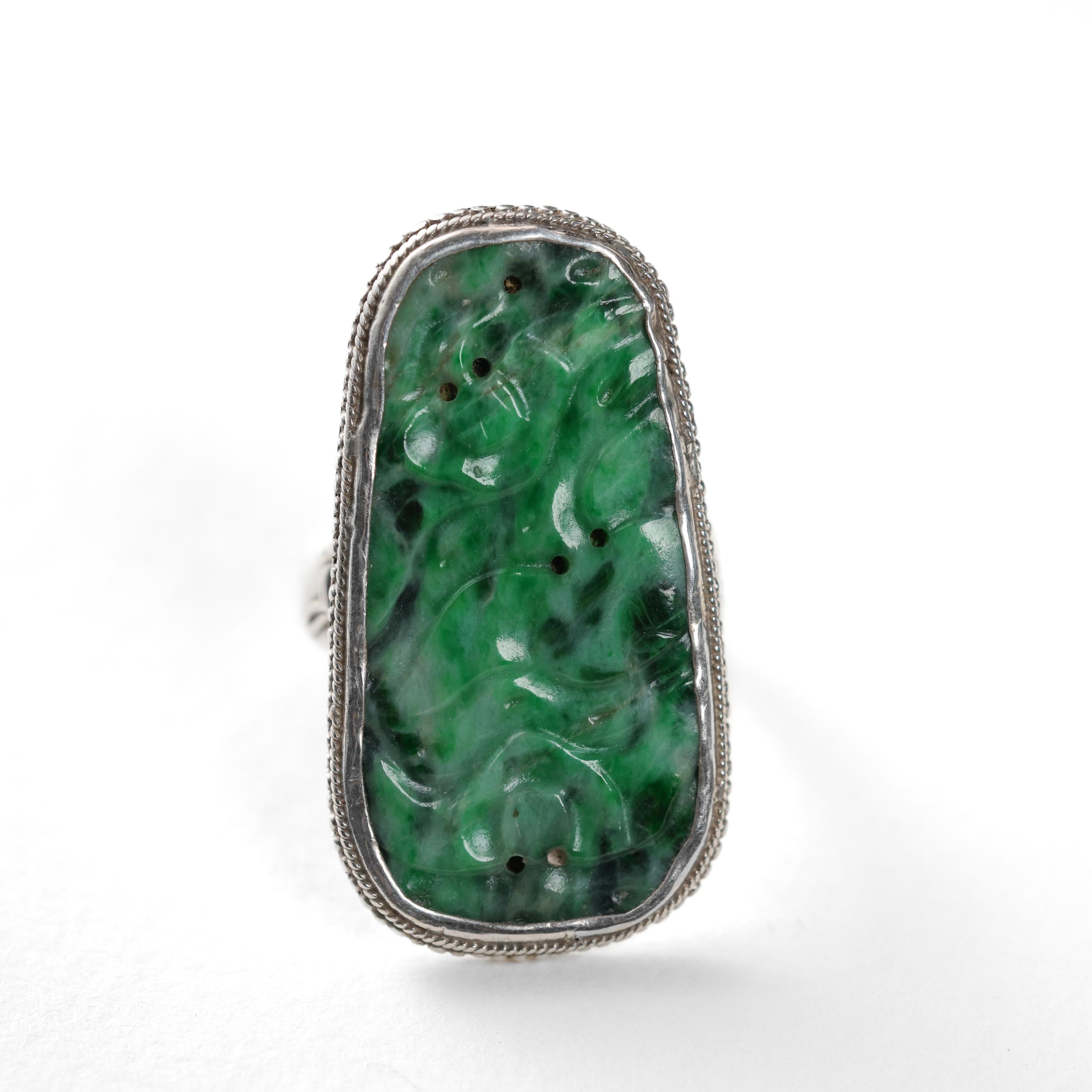 This Arts & Crafts era silver ring features a large (39 mm x 21 mm) richly saturated mottled emerald-green natural and untreated jadeite jade plaque that has been carved and pierced in a floral motif and set into a hand-fabricated silver mounting of