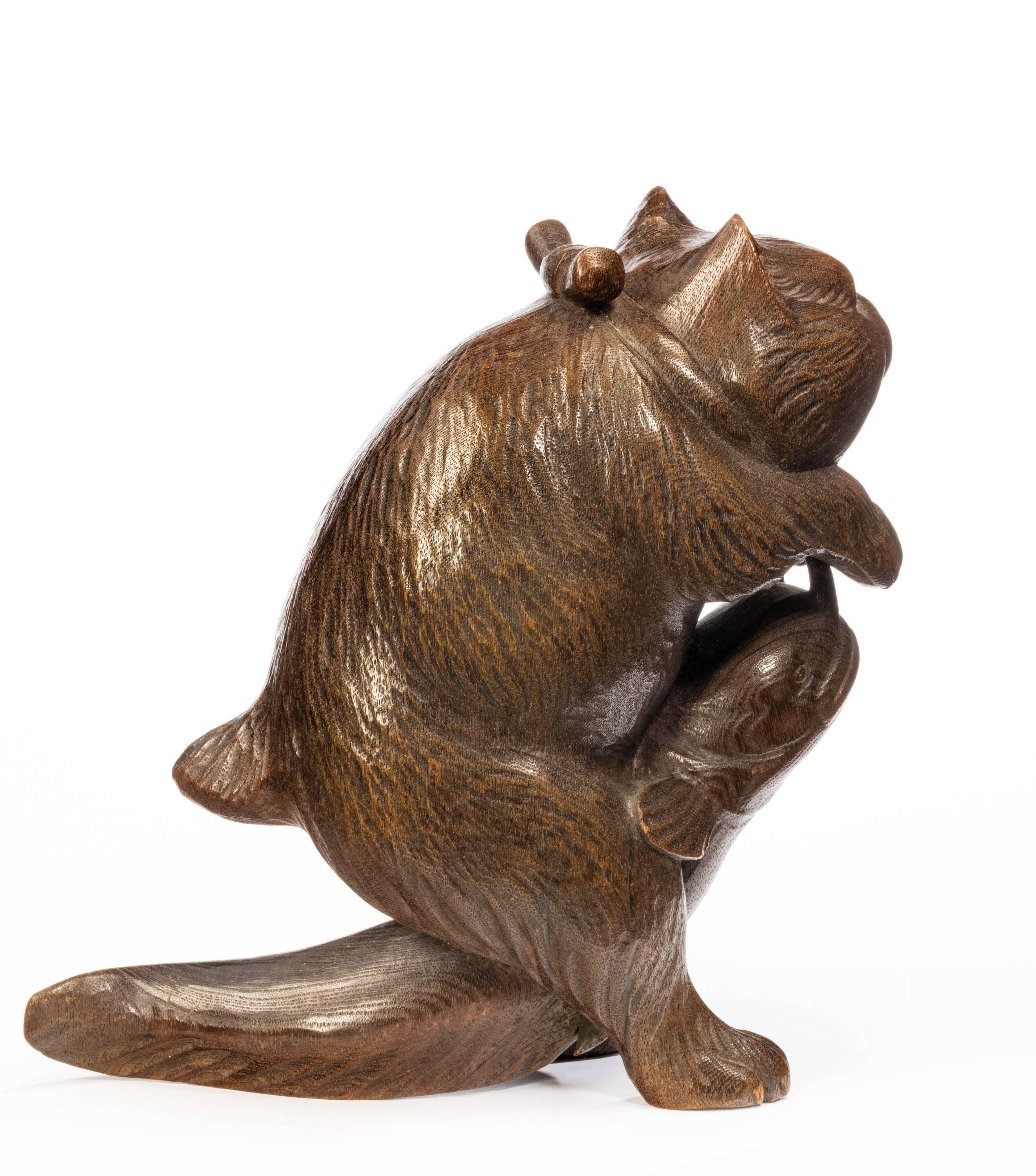 A well carved Japanese wooded figure of a cat playing with a dogfish. Signature tablet to the base.
 