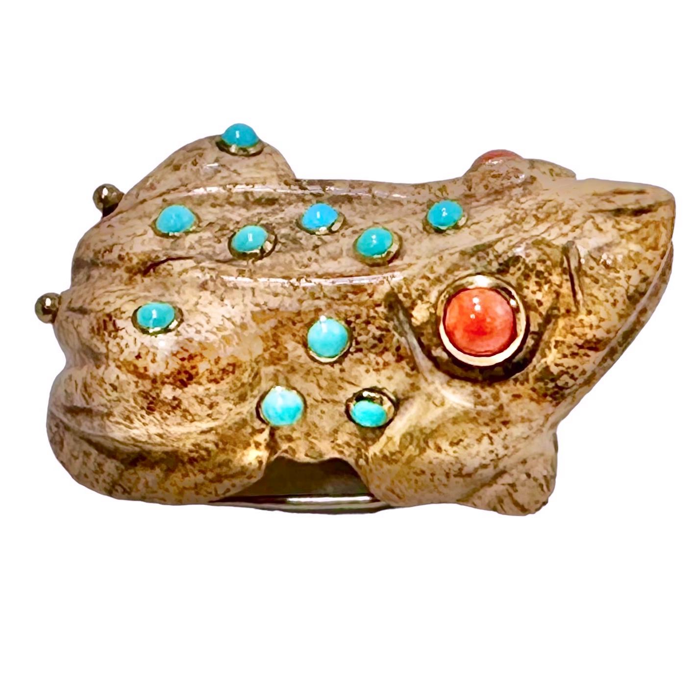 A carved, hardstone frog with a designer style. This friendly amphibian has two cabochon coral eyes that are bezel set in 18K yellow gold. In addition, it is detailed with 13 bezel set cabochon turquoise accents, and with gold beads on the