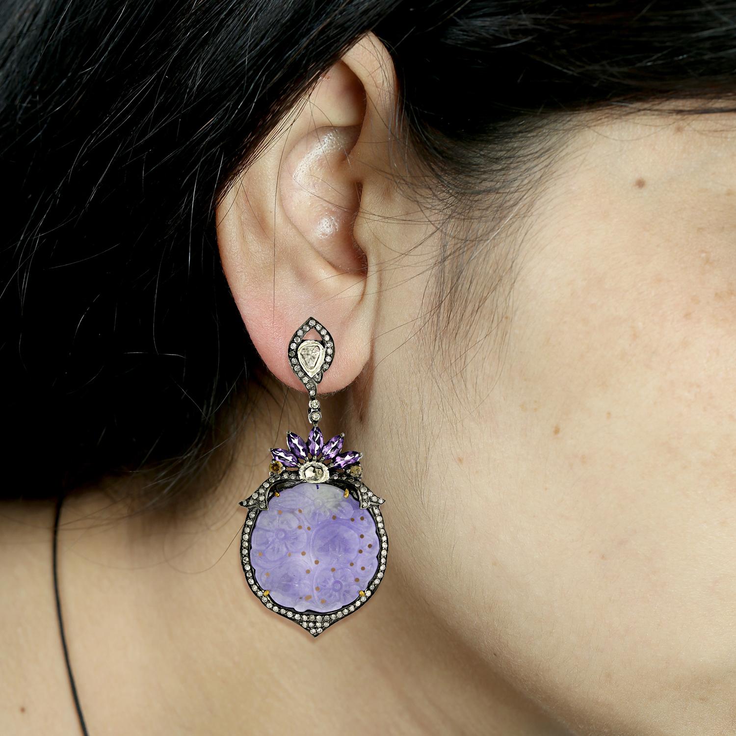 The awesome hues of this round carved lavender jade with marquee shape amethyst with diamonds around is so pretty that it will make you blush naturally when you wear it.
Closure: Push Post

18kt:1.08gms,Daimond: 2.67ct,slv:15.28gms,Amethyst:2.23ct,