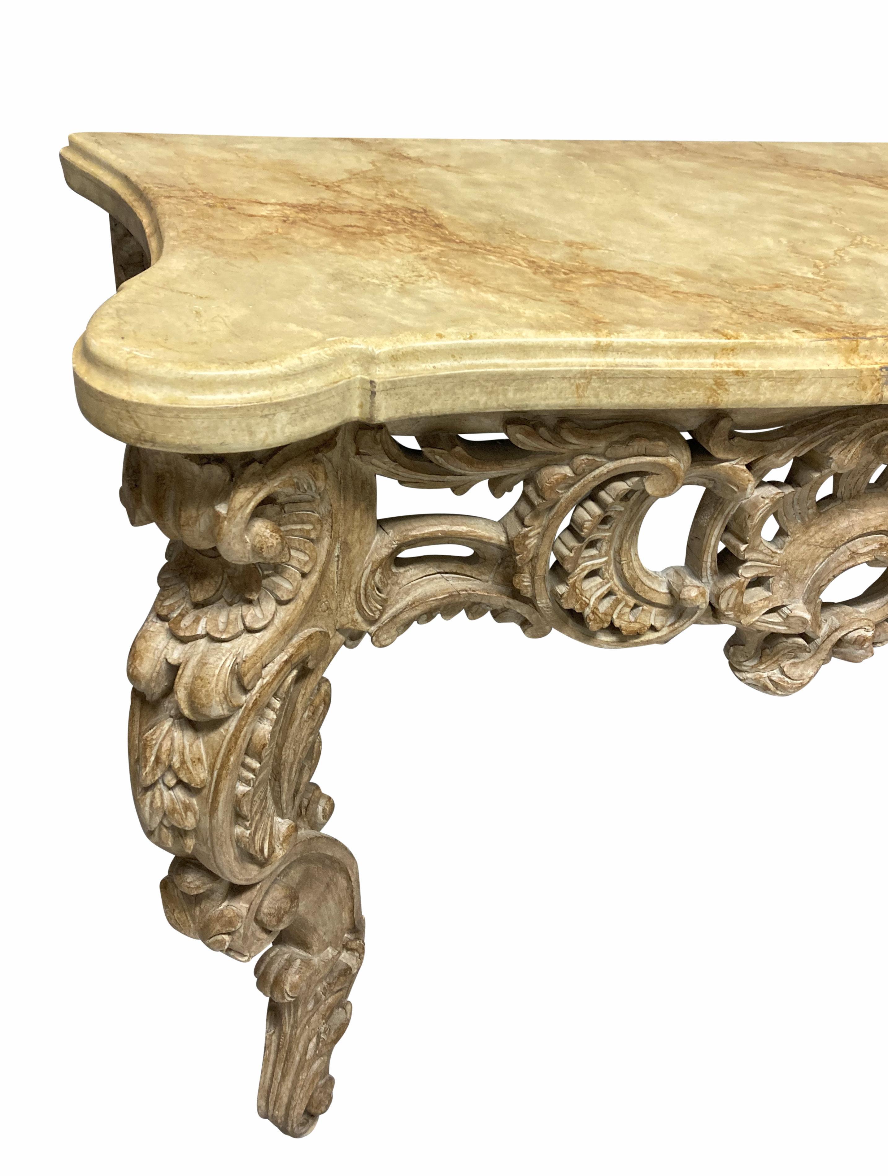 An Italian carved and limed fruitwood console table in the XVIII Century style, with a shaped faux marble top.