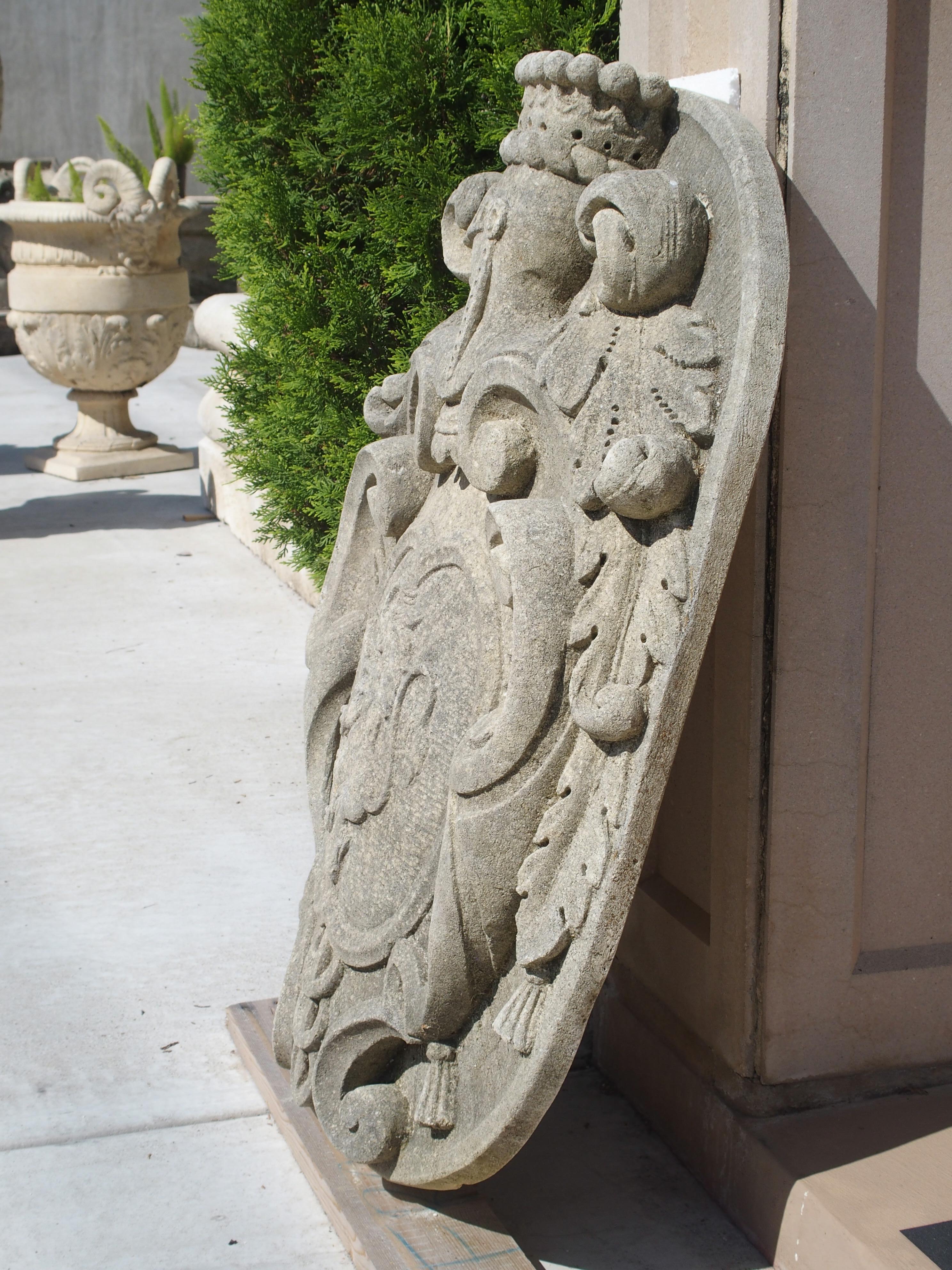 This large Italian limestone plaque is completely carved by hand (not cast), in relief and depicts a cartouche with a crowned helmet at the top. It is flanked by scrolling acanthus leaves and trailing acanthus leaves ending in tassels. The interior