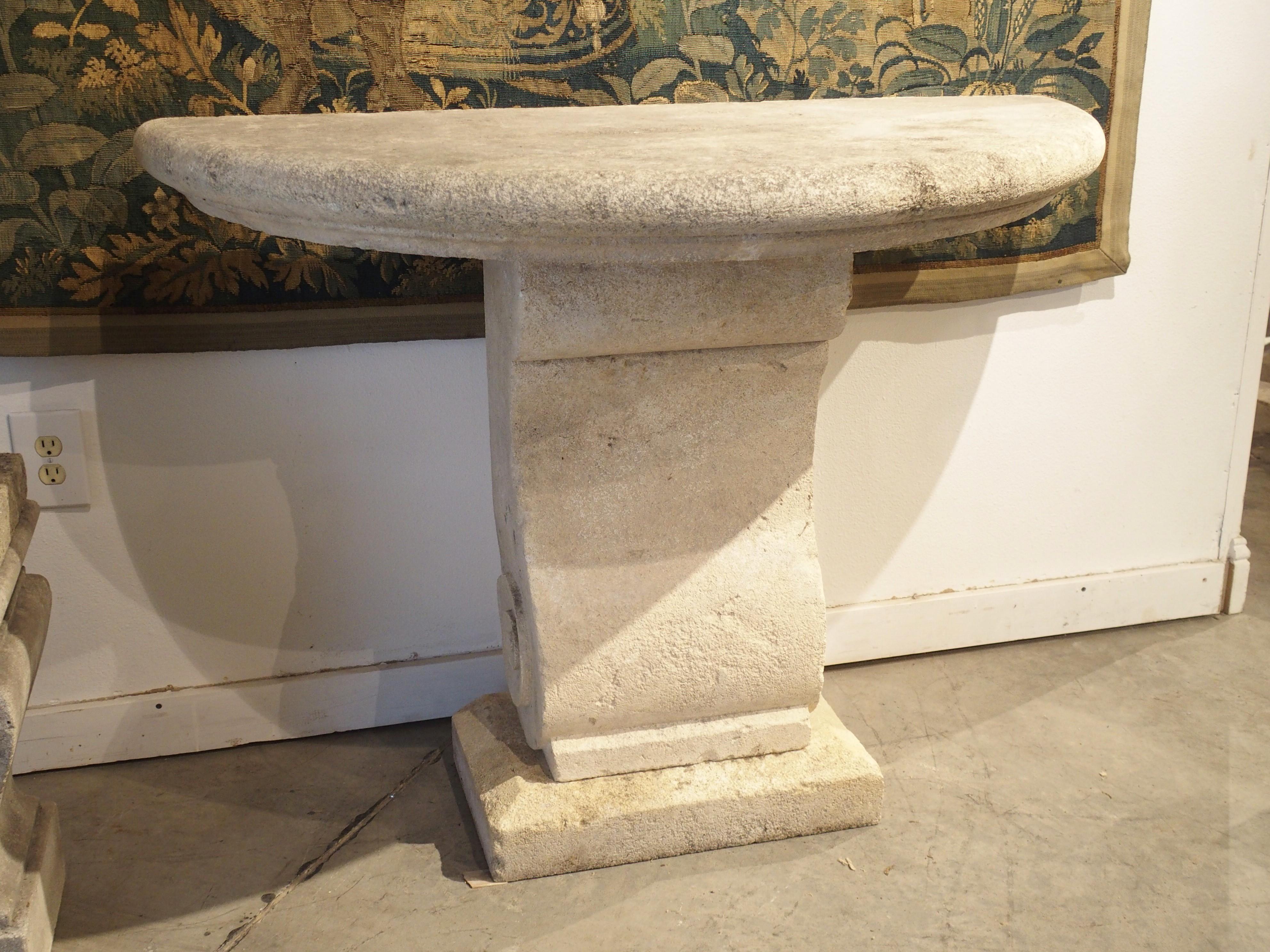 Hand carved in Provence, France, this limestone demilune console has a four inch thick top with a recessed carving above a cavetto molding. A corbel-like column sits beneath the top, supported by a rectangular plinth with beveled edges. The column