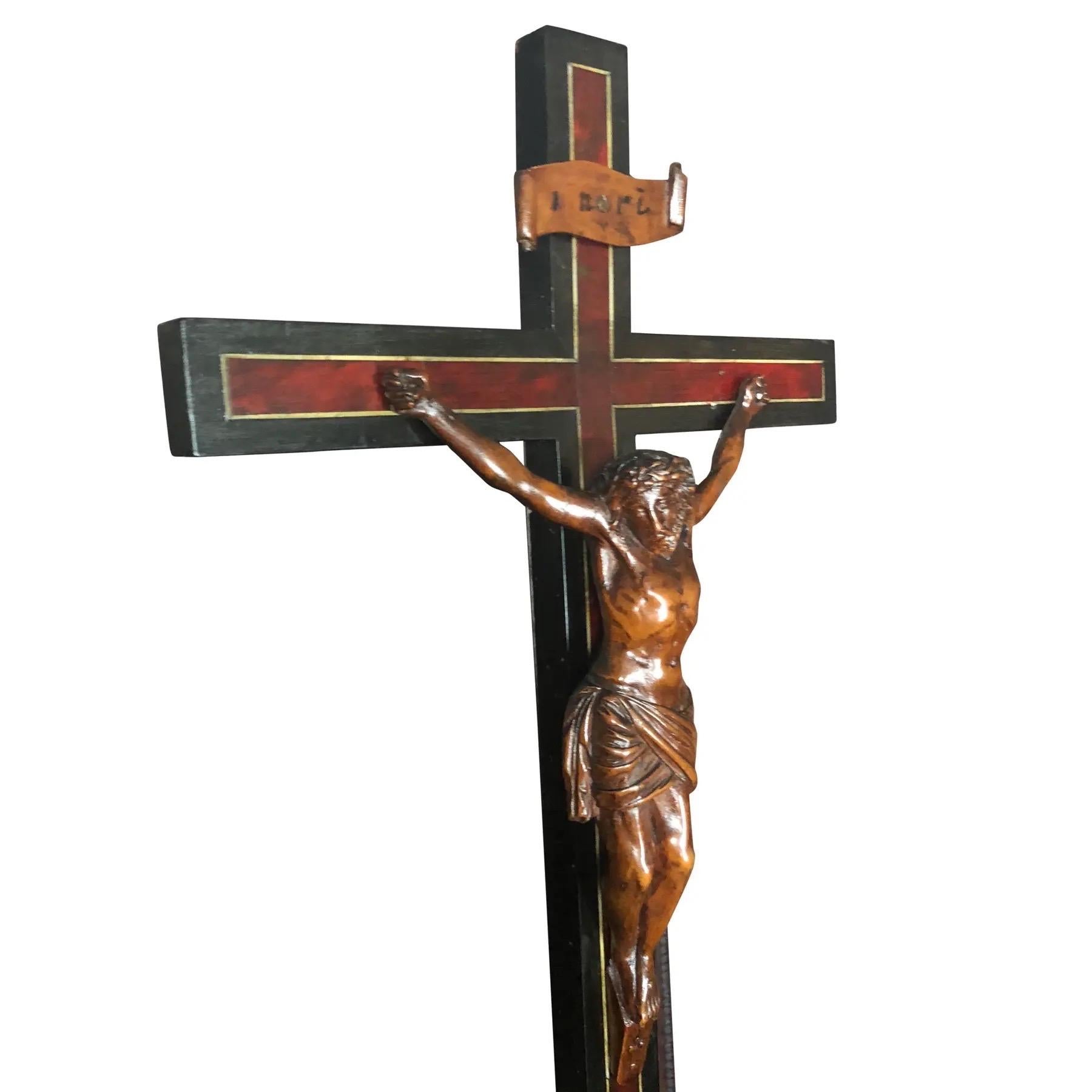 An intricate sculpture of Jesus on the cross. Jesus is finely carved from limewood on a limewood and ebonized mahogany cross. A richly beveled base is inset with limewood panels and stands on six round pad feet.