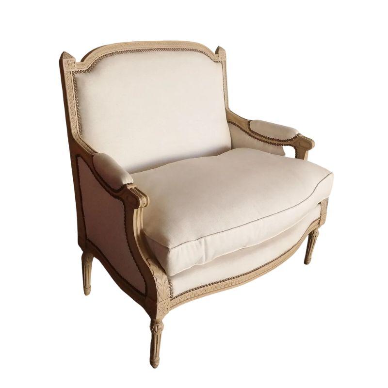 A vintage carved Louis XVI settee with cream cotton upholstery, tight back and removable down cushion seat. The French frame is carved with acanthus leaf and scroll detail. Fabric is detailed with nail head trim.