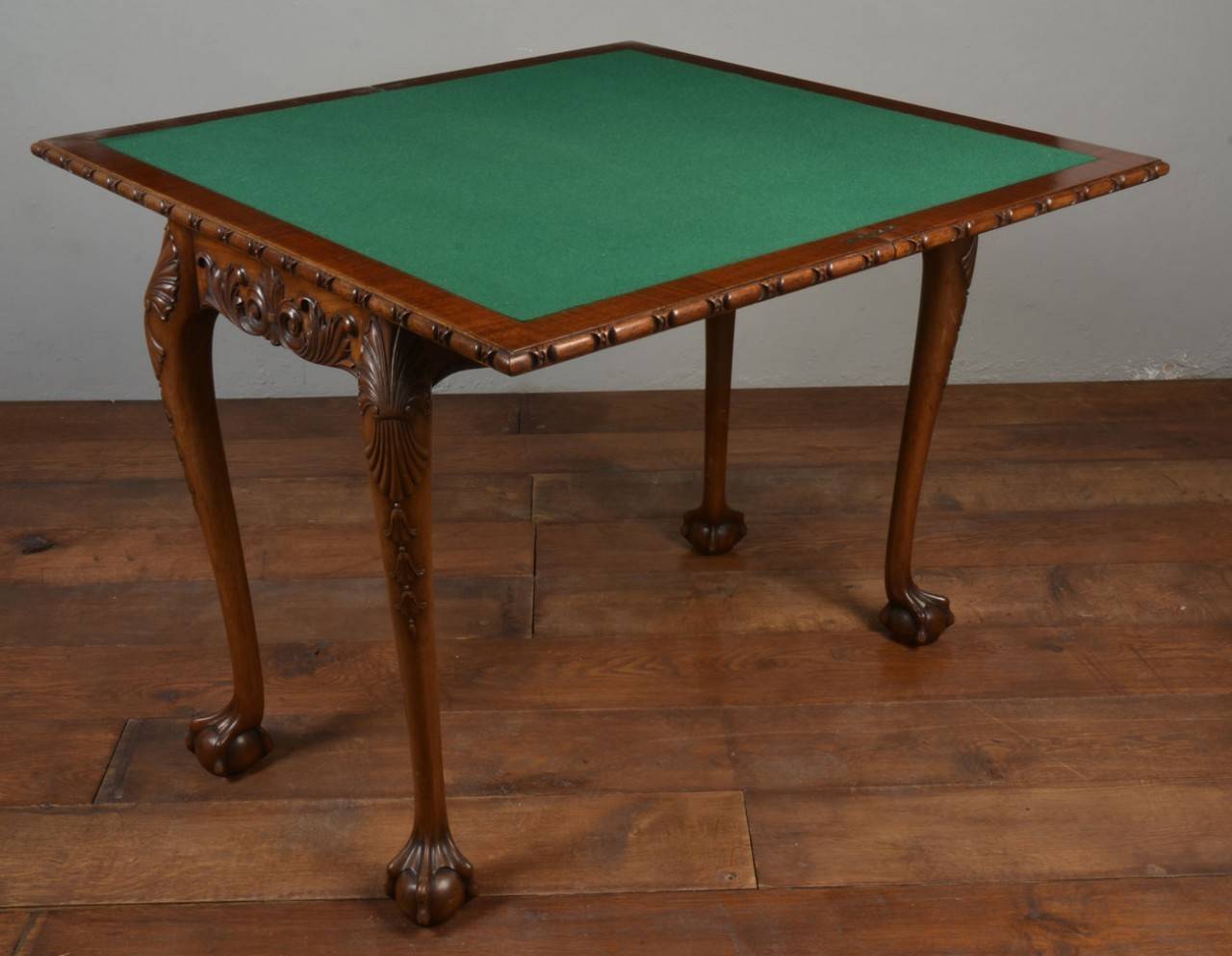 Chippendale style crossbanded mahogany fold over card table/ side table the large rectangular flame mahogany top opening to reveal inset green baize interior above a foliate carved apron and shell carved slender supports terminating in ball and claw