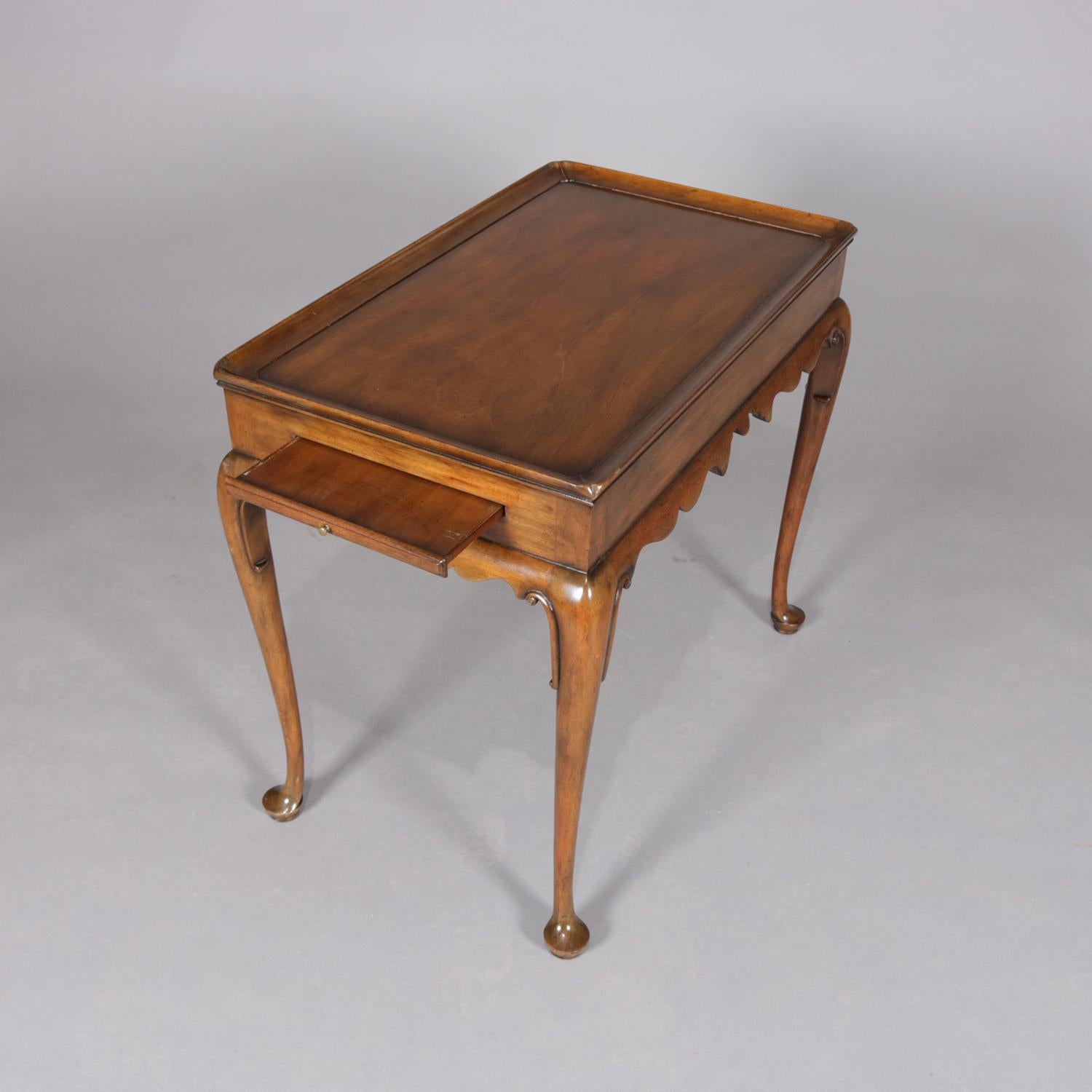 A carved mahogany Williamsburg tea table by Kittinger features top with full surround lip, pullout / pull-out side slide trays, scalloped skirt, and raised on cabriole legs terminating in pad feet, signed on base, 20th century.

***DELIVERY NOTICE –