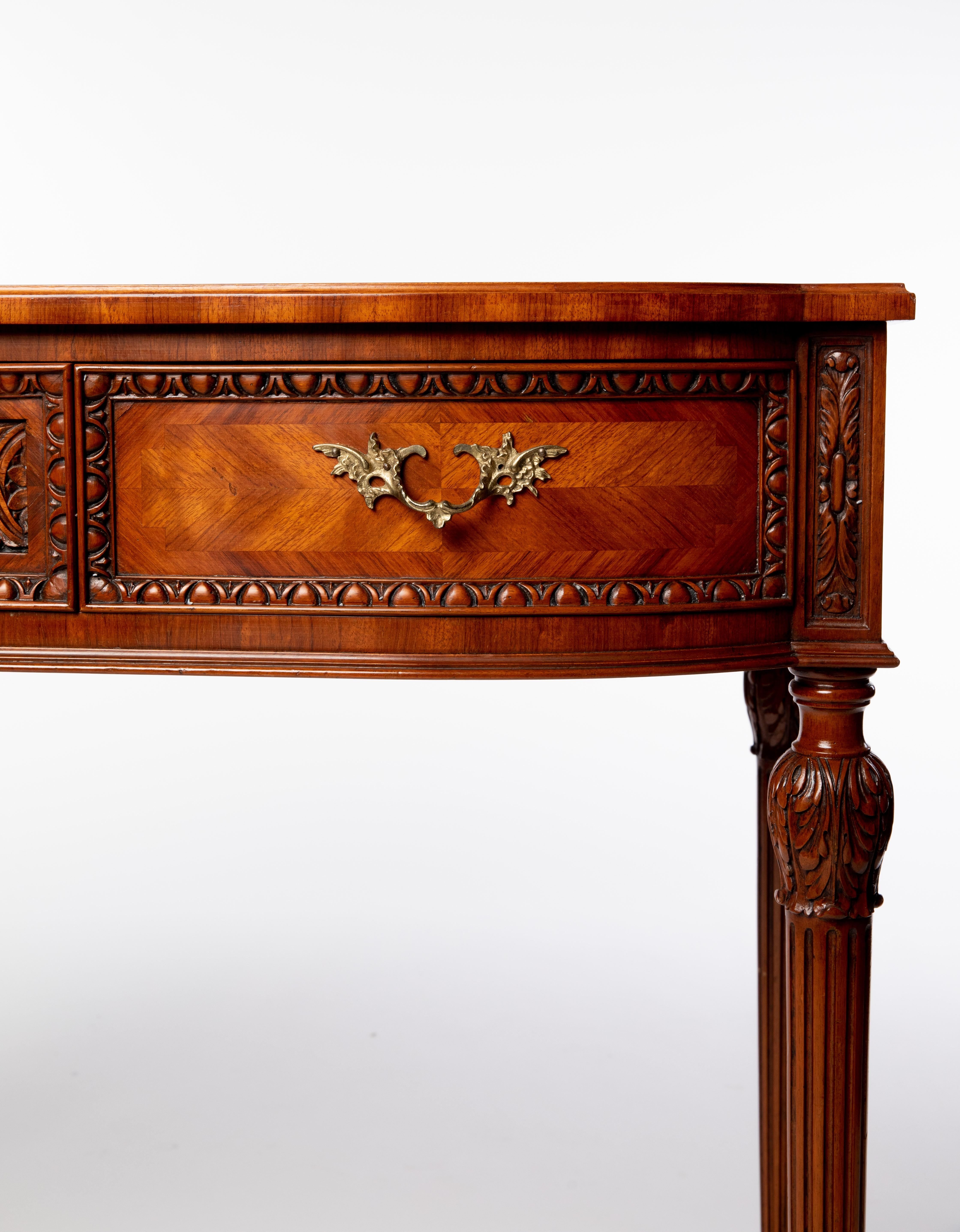 Carved mahogany console table, late 20th c., matched veneer top with banded inlay, over two drawers, rising on fluted tapered legs with carved acanthus caps.