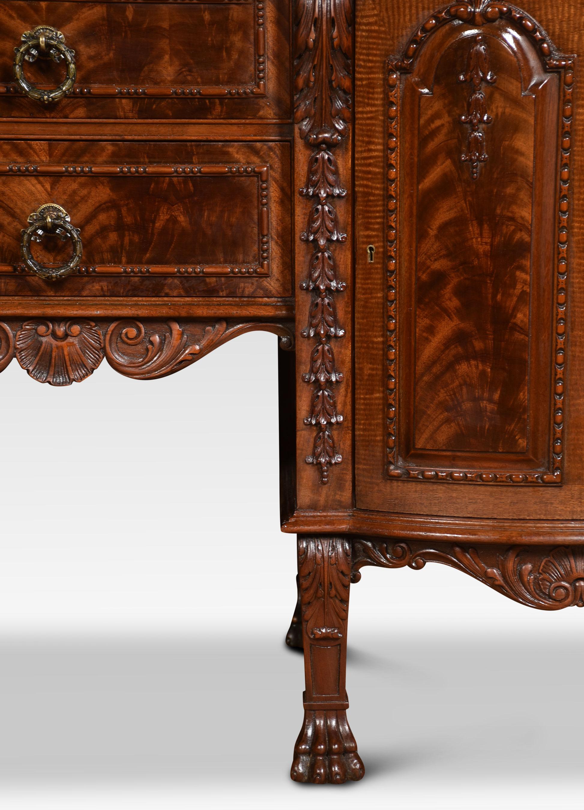 Carved mahogany sideboard the large rectangular inverted breakfront top and molded edge above two central drawers with brass tooled handles flanked by arch panel cupboard doors opening to reveal the fitted interior. All raised up on short legs