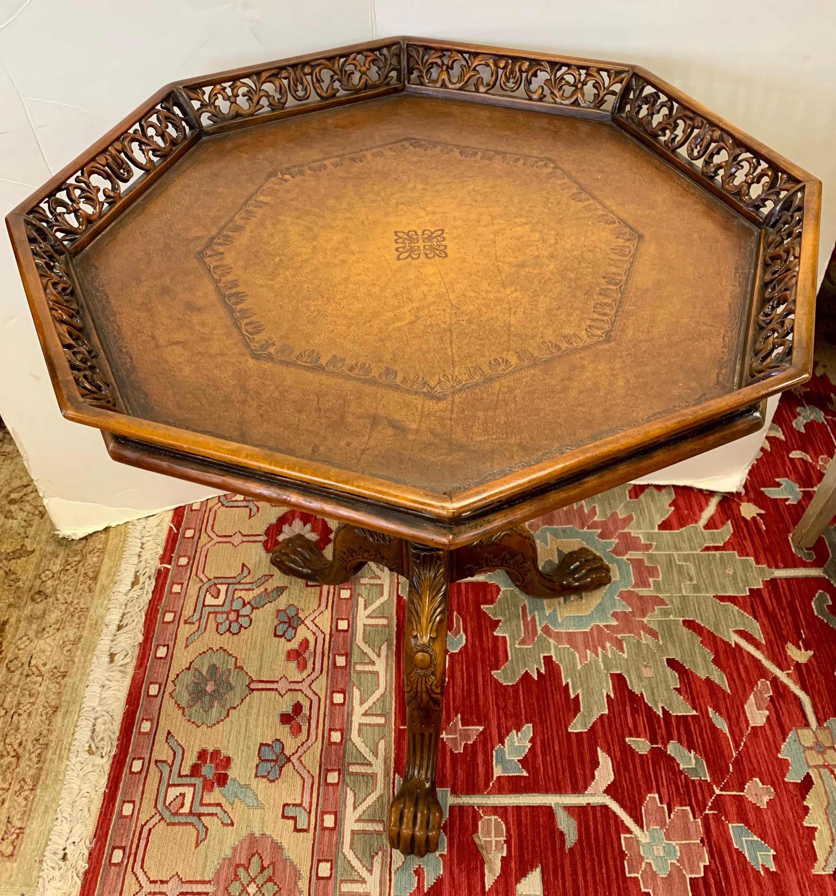 Elegant mahogany pie crust table with hand carved raised gallery and leather top. Resting on a carved center baluster with tripod claw and ball feet.