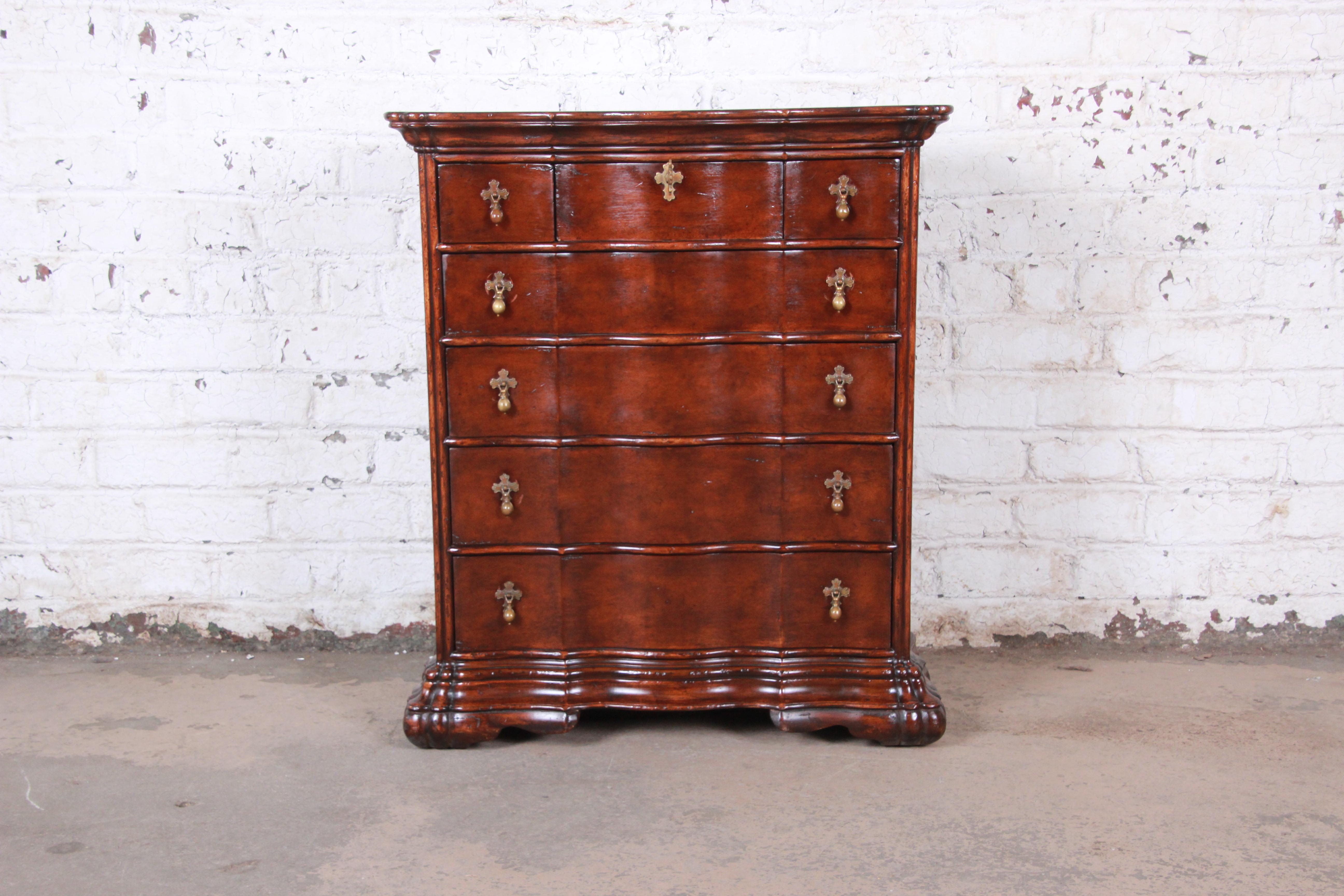A gorgeous vintage carved seven-drawer mahogany chest of drawers. The dresser features stunning mahogany wood grain and original brass teardrop hardware with cross-shaped design. It offers ample storage, with three small drawers at the top and four