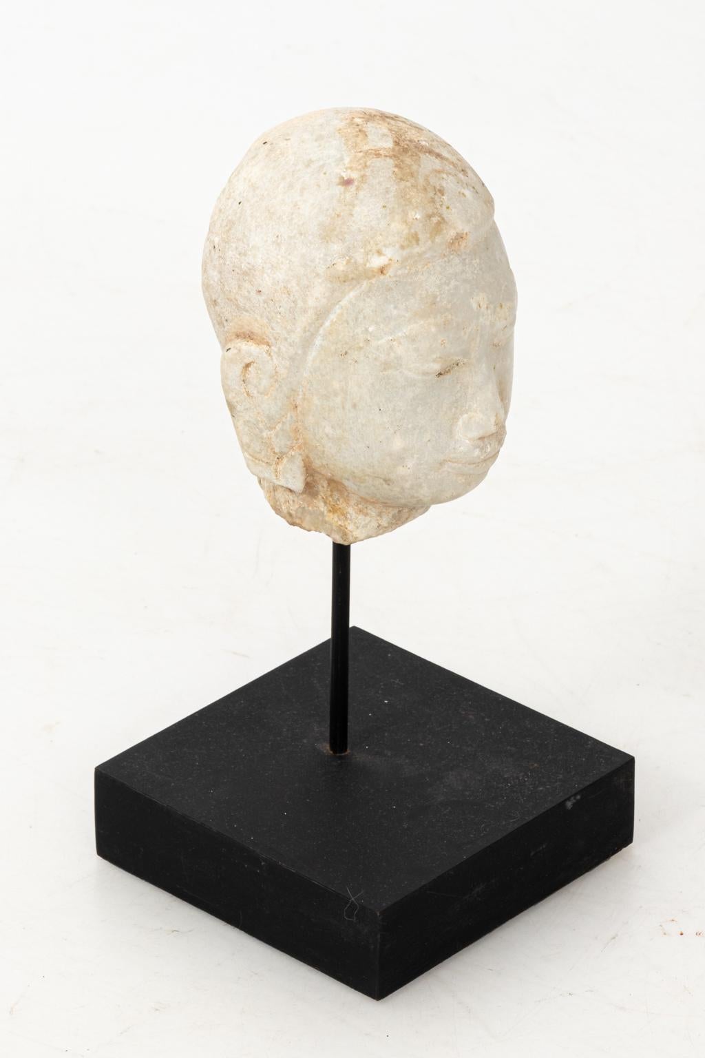 Carved marble Buddha head statute on stand. Please note of wear consistent with age including a distressed finish.