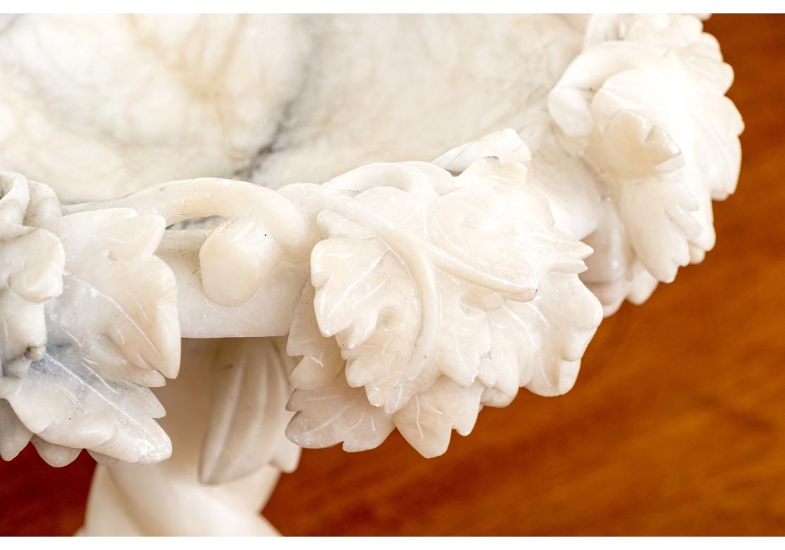 A finely carved compote with a deep overhanging rim with grape clusters on the serpentine vine. Triple swirled dolphins with articulated curved tails form the support raised on a triangular base. Likely Italian. 

Dimensions; 11 1/4