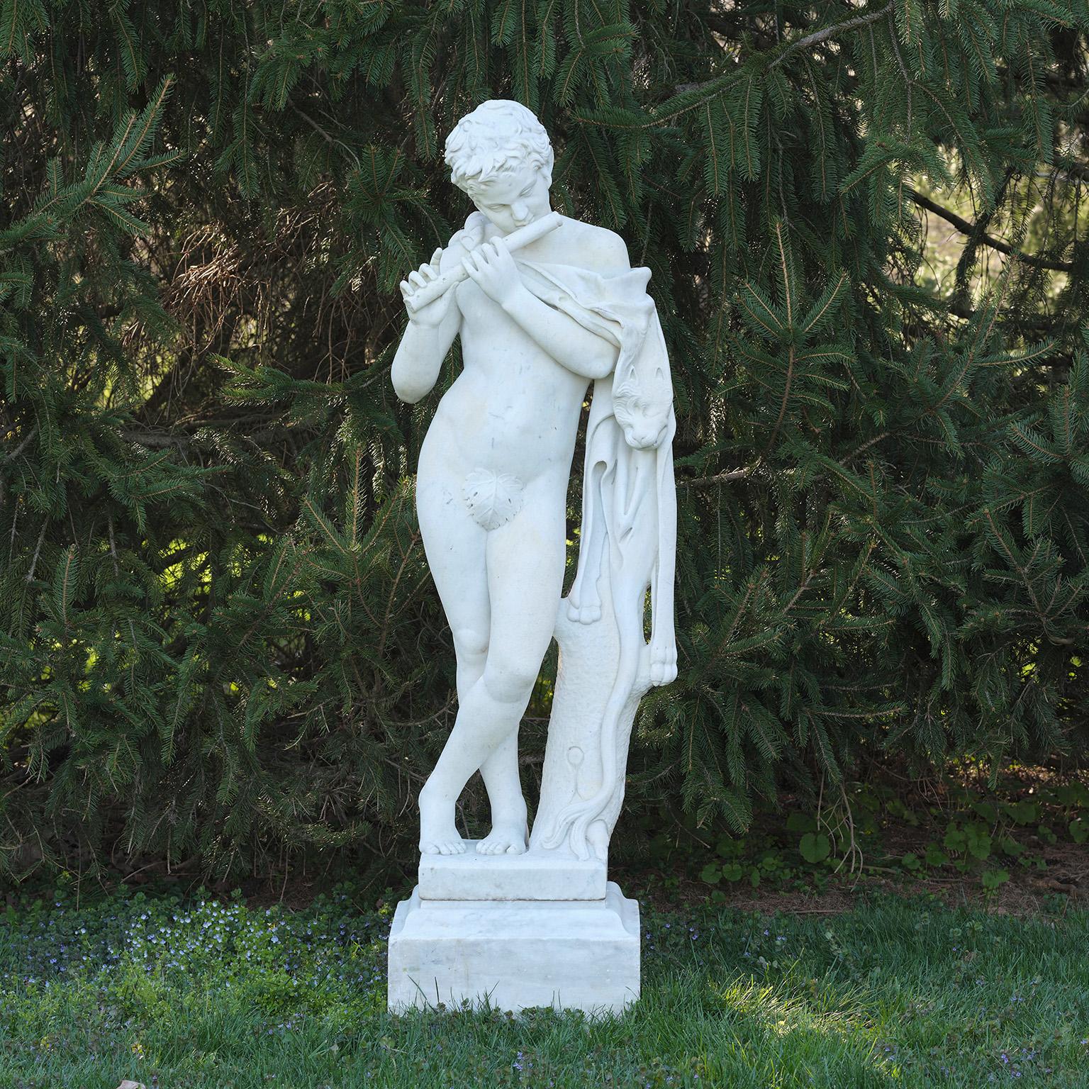A carved marble figure of a faun playing the flute, the figure’s head is tilted to meet the flute in playing position, with left leg crossed in front of the right leg, and with left hip leaning slightly upon an adjacent tree stump, the figure draped