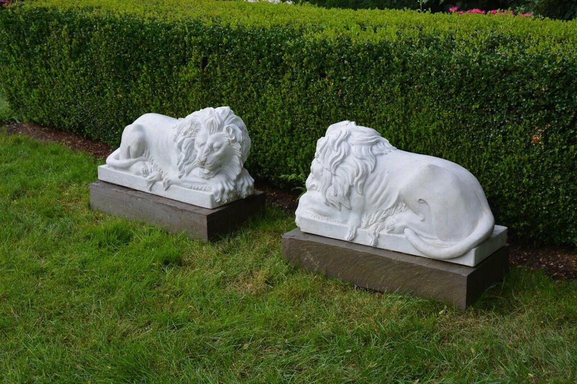 A pair of carved marble lions, inspired by a model by Bertel Thorvaldsen, one lion awake, one asleep with eyes closed, both with clawed front paws extending beyond integral base, Asian, circa 1990. Measures: 19 ins. high, 27 ins. long, 15 ins. wide