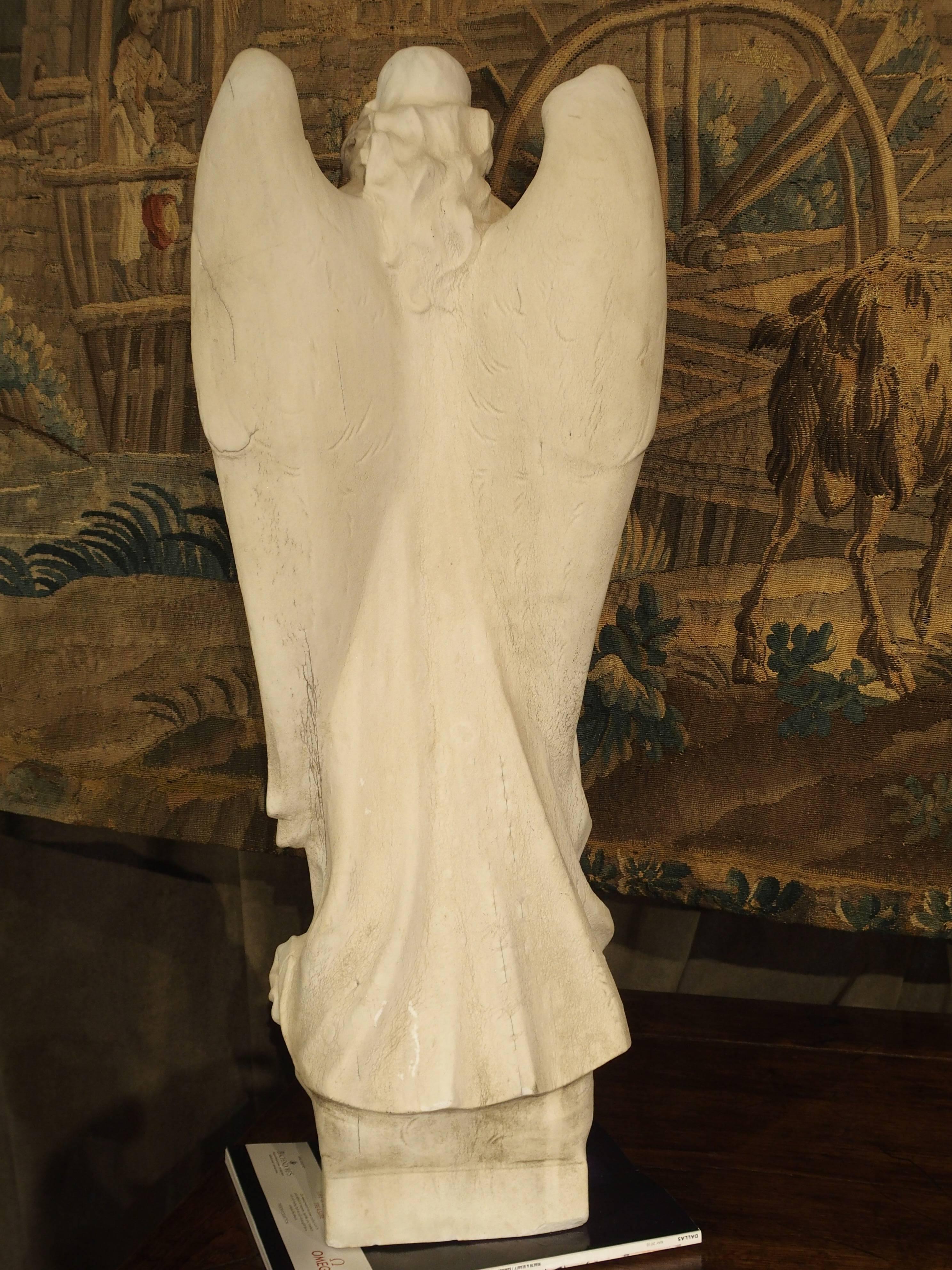 This is a hand-carved marble statue of an Angel holding a bouquet of flowers that stands over 34 inches tall. She is wearing a long, draped robe with stems of flowers flowing down her robe from the bouquet. Her wings are closed, falling gracefully