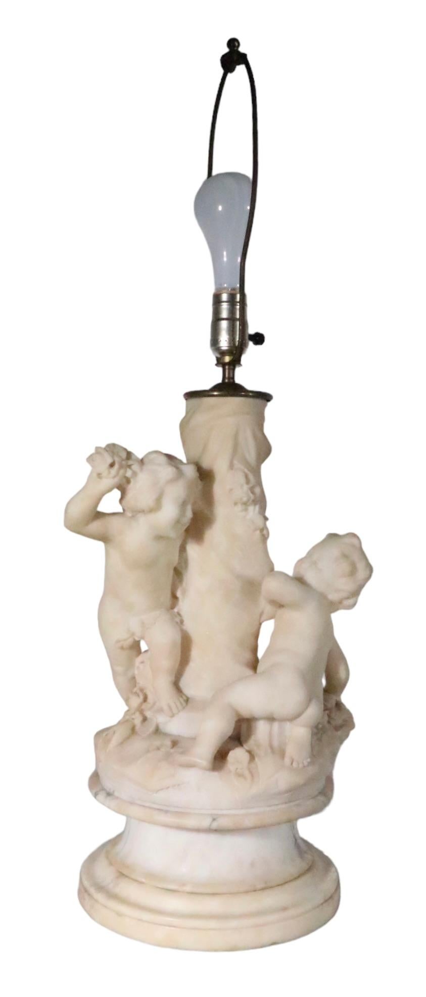 Lampe de table en marbre finement sculpté présentant deux figures de cupidon jouant autour d'un poteau central. La lampe est en très bon état d'origine, propre et fonctionnelle, ne présentant qu'une légère usure cosmétique, normale et cohérente avec