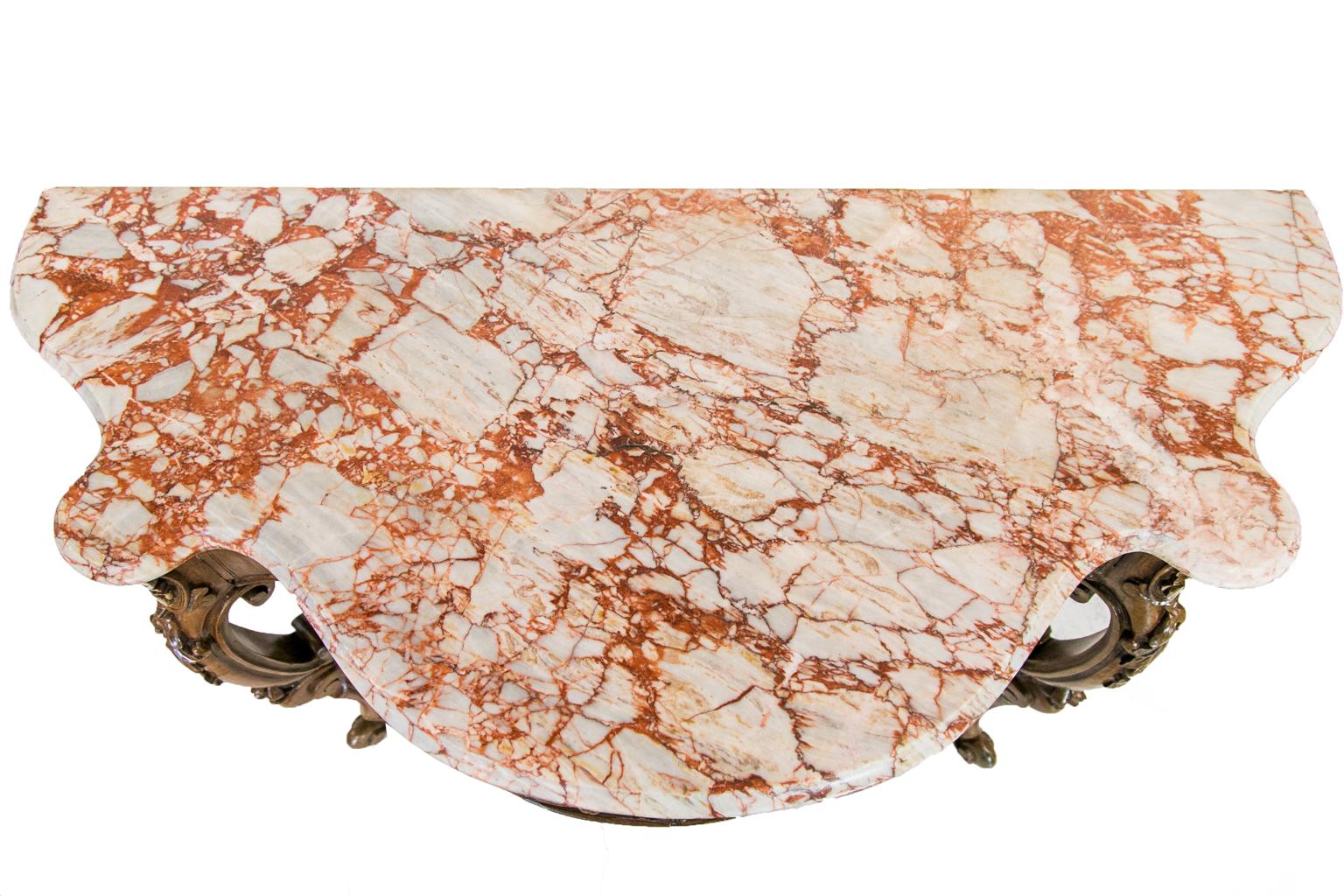 This carved marble-top console table has a double serpentine shaped marble. The marble edge is ogee shaped. The front and side aprons have flowers, vines, and leaves carved in high relief. The legs have double reverse carved volutes and have
