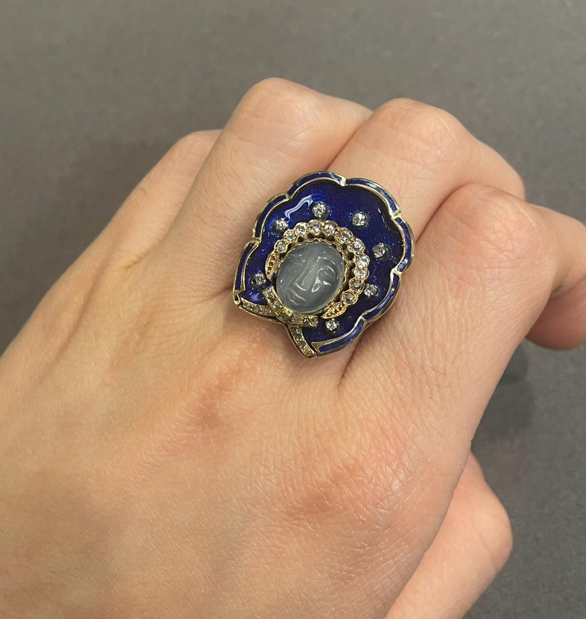 Carved Moonstone Ring

A yellow gold ring featuring a carved moonstone face at the center, accented with round cut diamonds. The outer section is set with blue enamel. 

Ring Size: 6
Complimentary resizing 
Metal Type: 14 karat gold