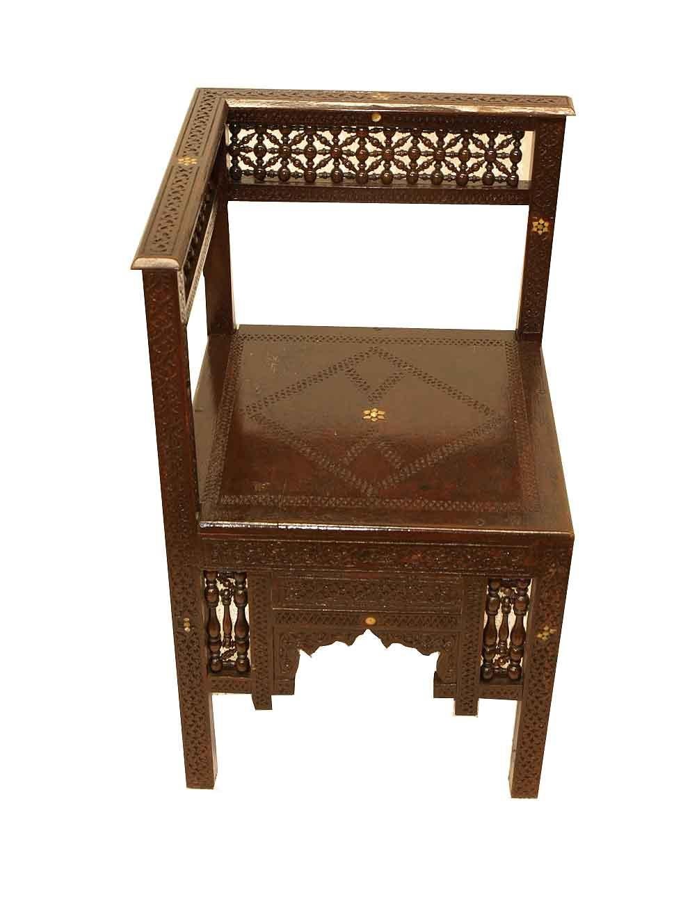 Geschnitzter marokkanischer Eckstuhl, die geschnitzte Kammleiste mit eingelegten stilisierten Perlmuttsternen über der Rückenlehne mit einer Vielzahl von miteinander verbundenen gedrechselten kleinen Spindeln. Alle vier Seiten des Stuhls und des