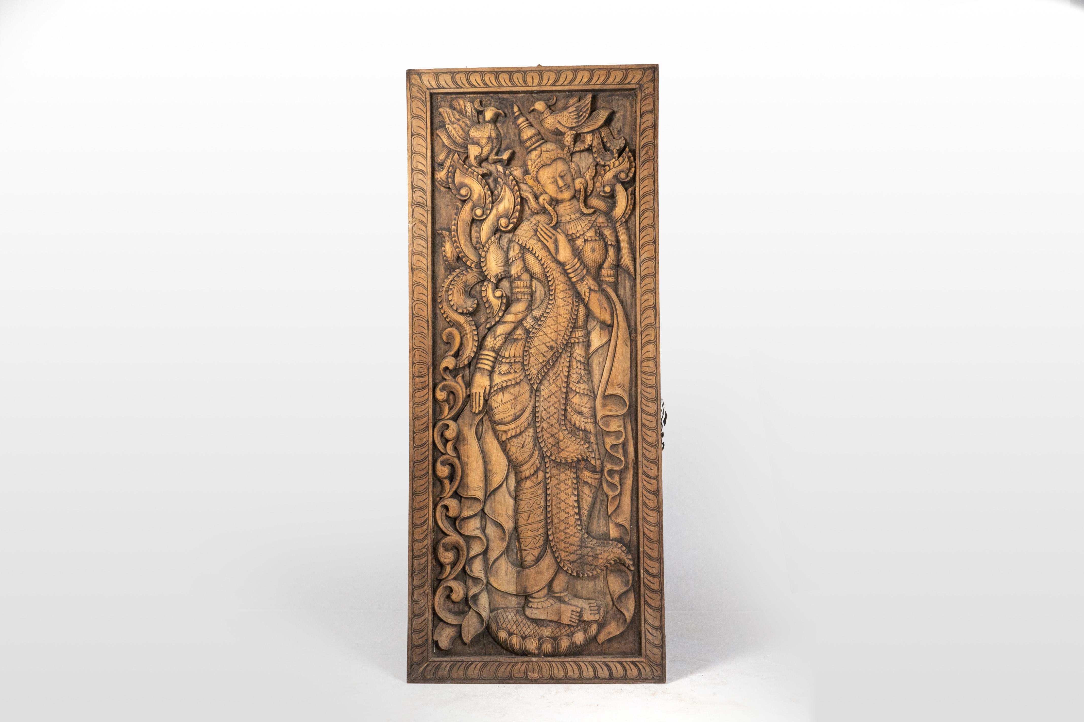 This exquisite hand-carved teakwood mural panel from Myanmar, crafted in the early 21th century, showcases a stunning depiction of a Burmese nat, or apsara. The panel, a substantial 3 inches thick, depicts the apsara dressed elegantly in traditional