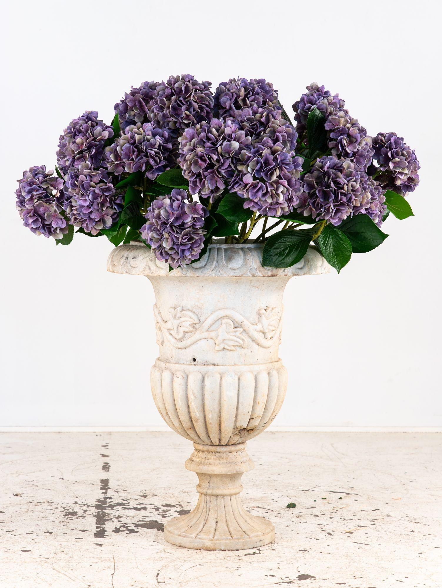 A carved Italian marble urn in the Neoclassical style, dating to the early 20th century. The lip is decorated with a classic egg and dart pattern, while the body features an elegant, repeating leaf and vine motif in deep relief. The fluted base adds