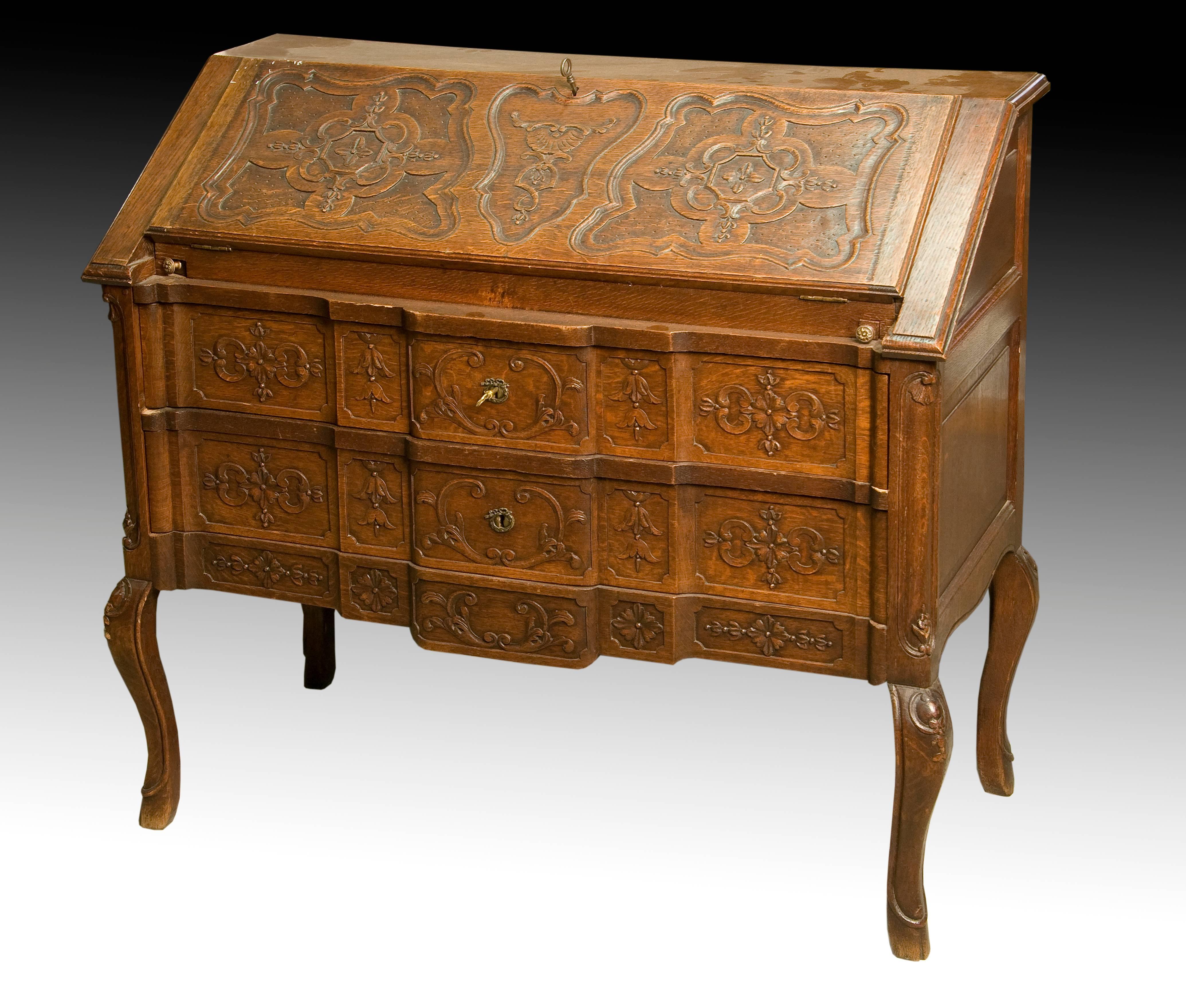 Desk with three drawers to the front that has slightly curved legs and a carving centered on the front of the furniture based on simple plant elements and moldings with curves and counter curves, inspired by the Rococo. This style also influences