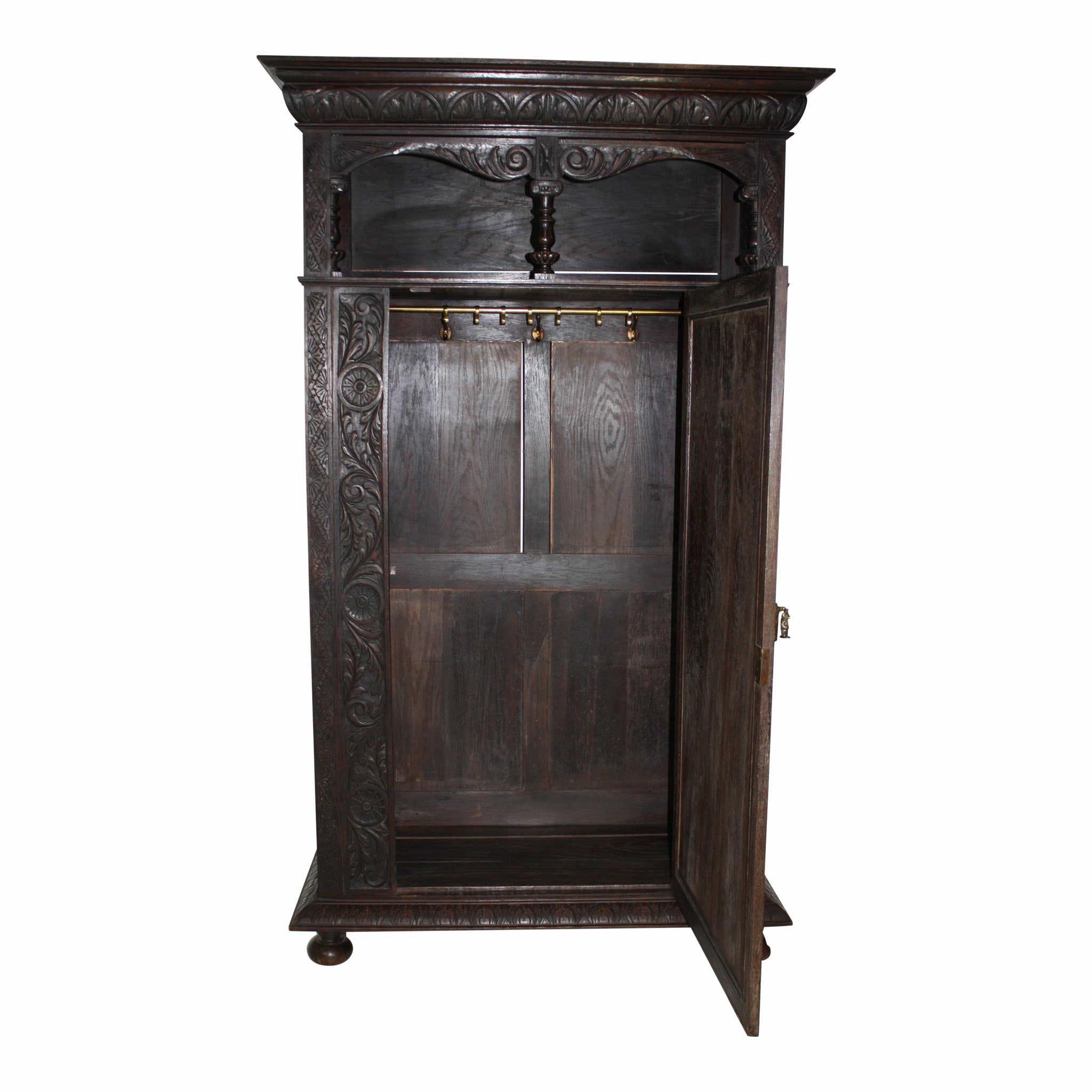 Providing generous storage and an upper display niche, this oak armoire is beautifully carved with scrolled acanthus leaves and flower heads enclosed in circles. Behind the single door, the armoire has a brass rod with seven suspended hooks. Three