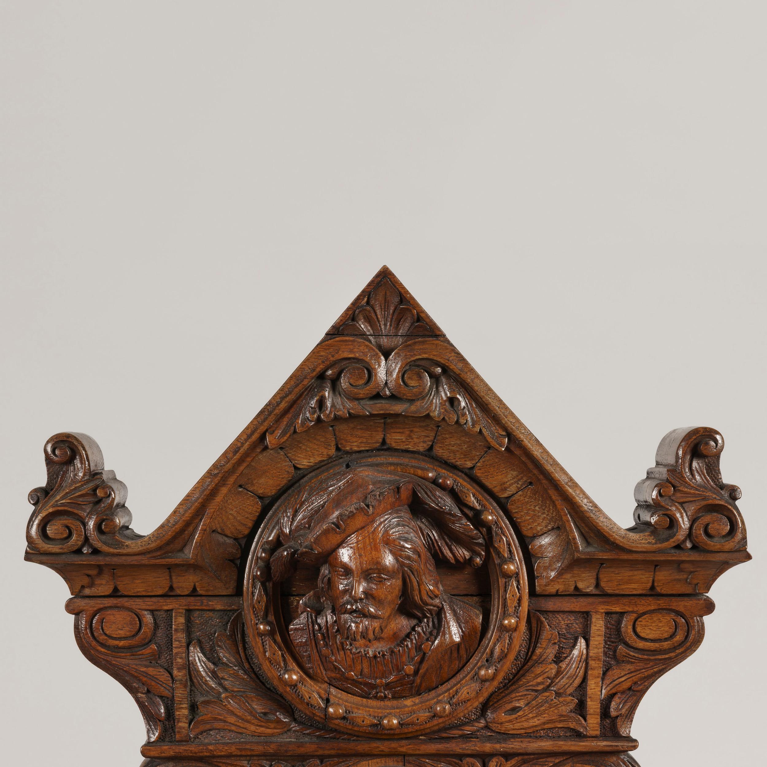 The barometer, of aneroid type, signed by the maker and having a thermometer above is house within an extensively carved 'banjo' form case, incorporating fruits and foliates, with a bust of a hatted man from the Troubadour period. Inscribed on the
