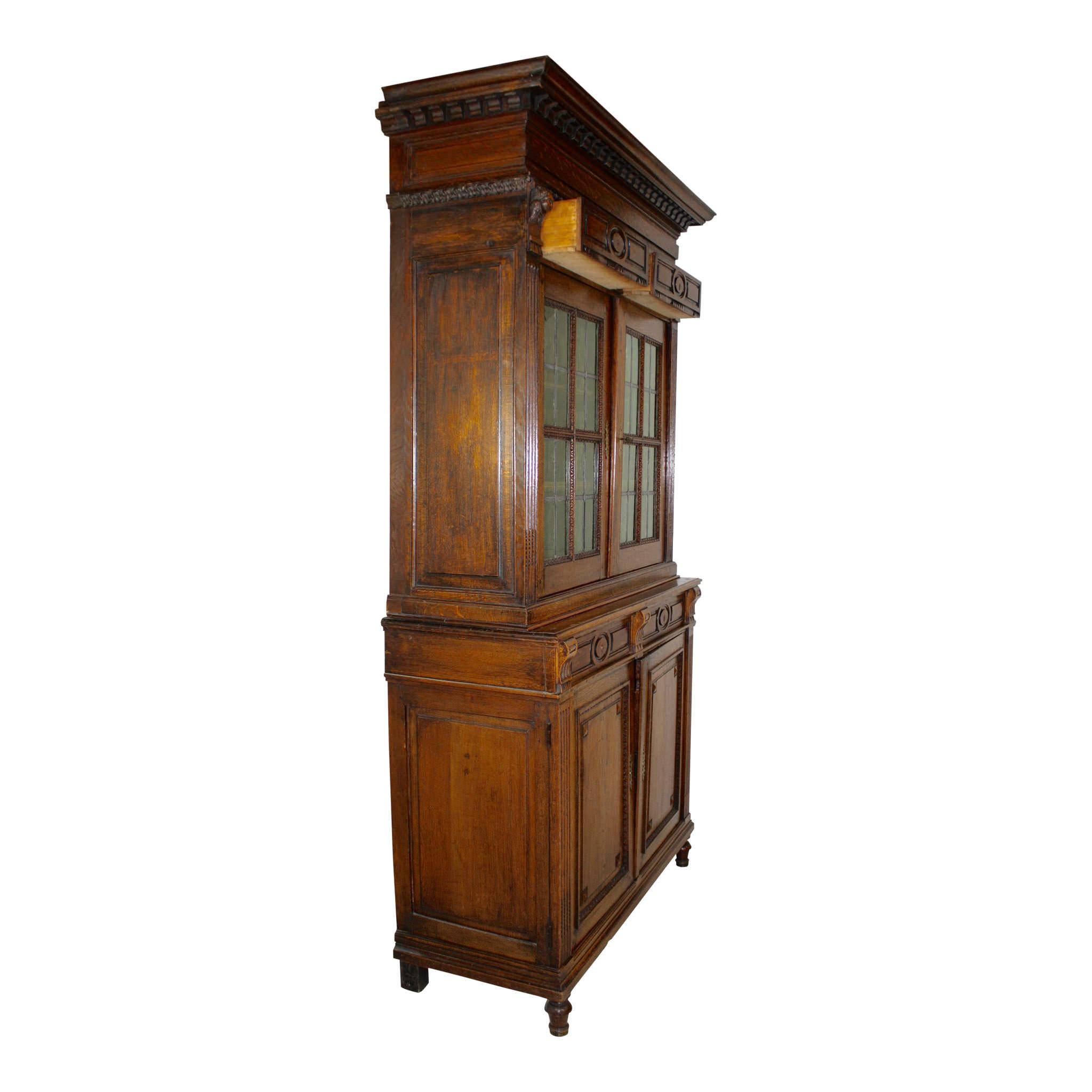 This double bodied, oak buffet features original, gold-tinted, glass panes on the upper doors and raised panels on the bottom doors. The shelving inside is adjustable. Dentil crown molding at the top rises above two surprise drawers, perfect for