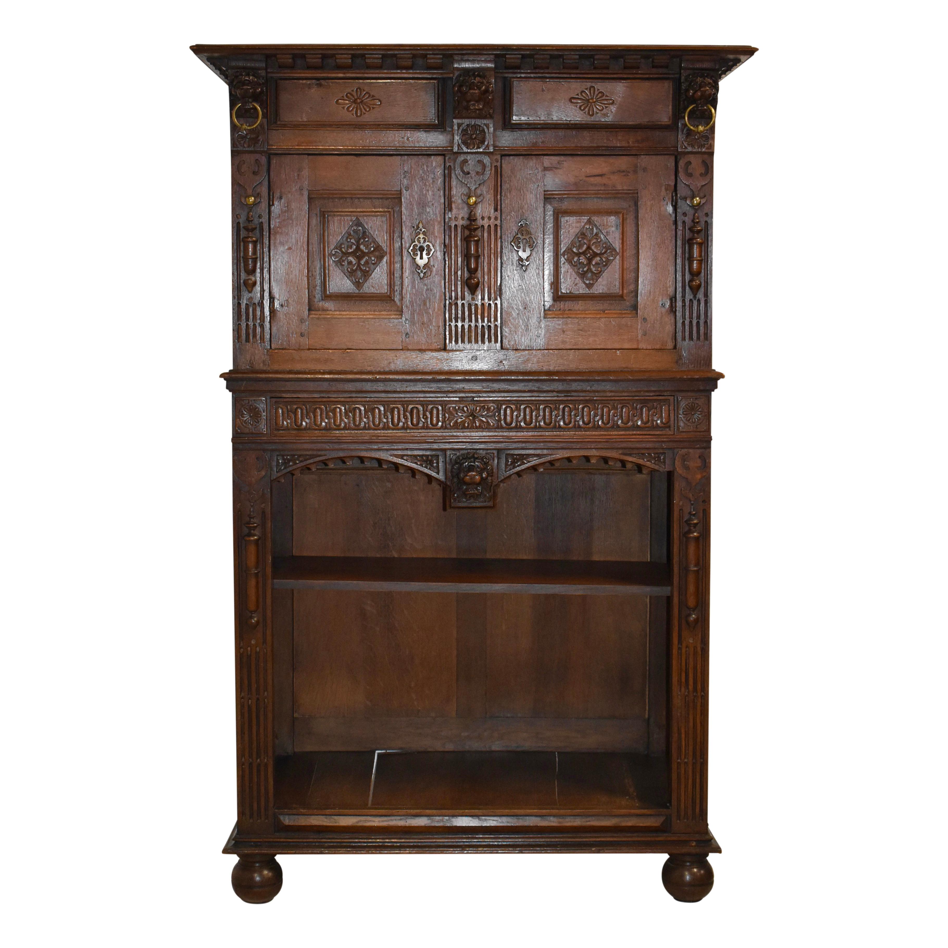Elegant but not too heavily carved, this oak cabinet showcases a dentil cornice, two top drawers flanked by lion mask carvings at the sides and between the doors, double doors flanked by decorated fluted panels, an open lower shelf, raised panels