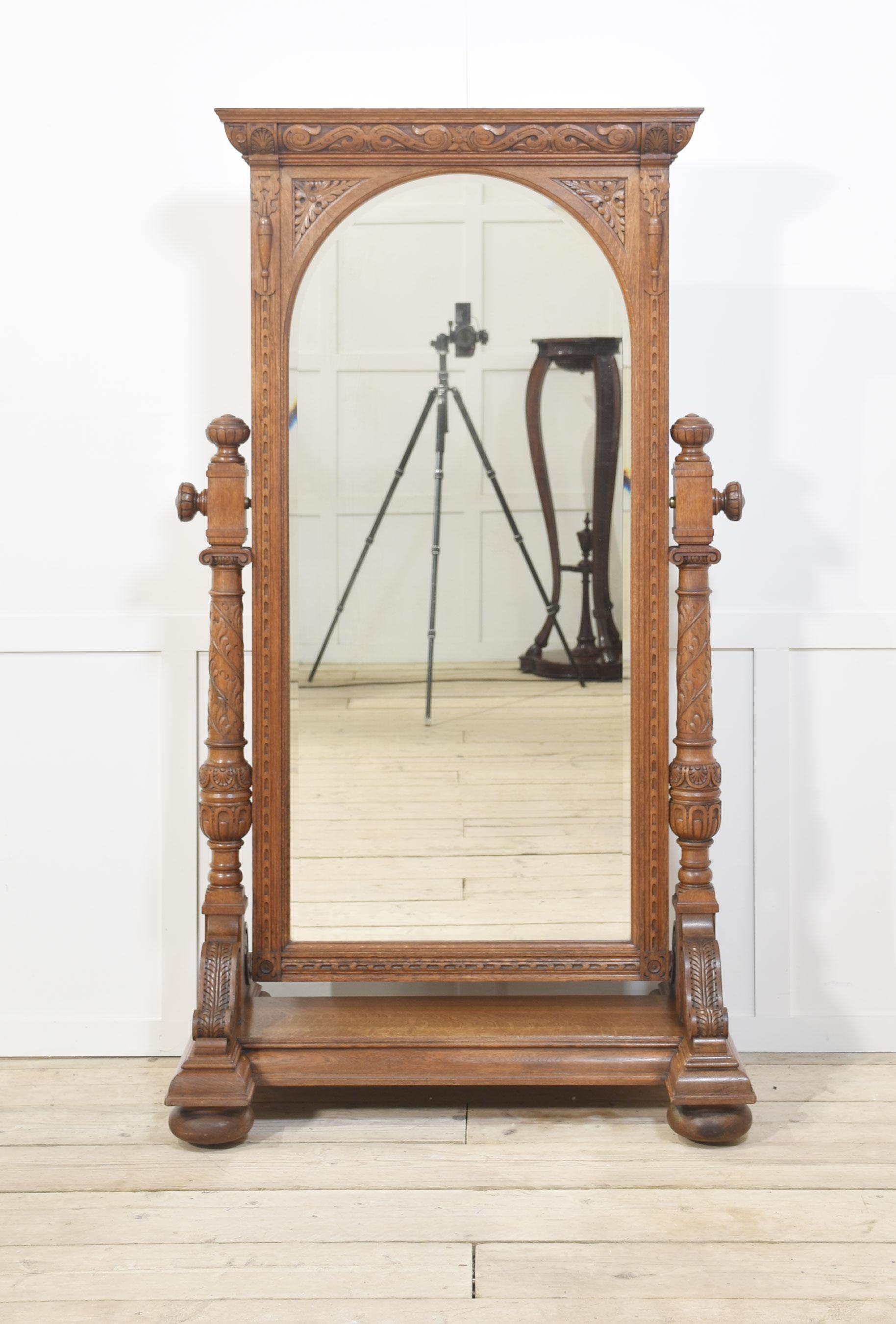 Large oak cheval dressing mirror having scrolling cornicing above an arched bevelled mirror plate and fluted frame, supported by a pair of architectural form columns over an inverted breakfront base with acanthus corbels and large compressed bun
