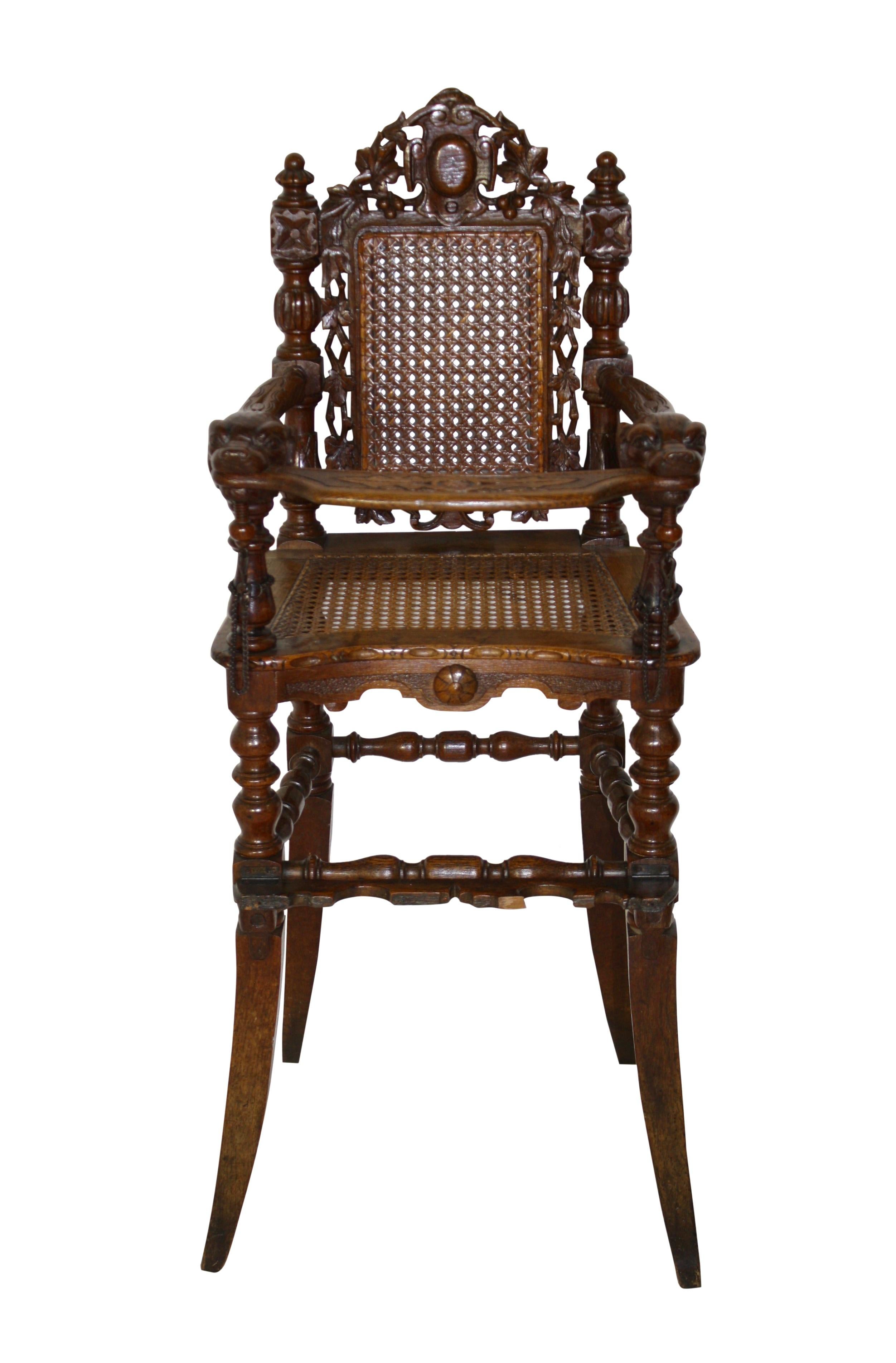 This adorable child's chair looks like the seat of honor. Turned and blocked stiles capped with knob finials secure a caned back with a pierced frame of carved grapes on a vine flowing down around a center medallion. Carved dogs' heads at the end of
