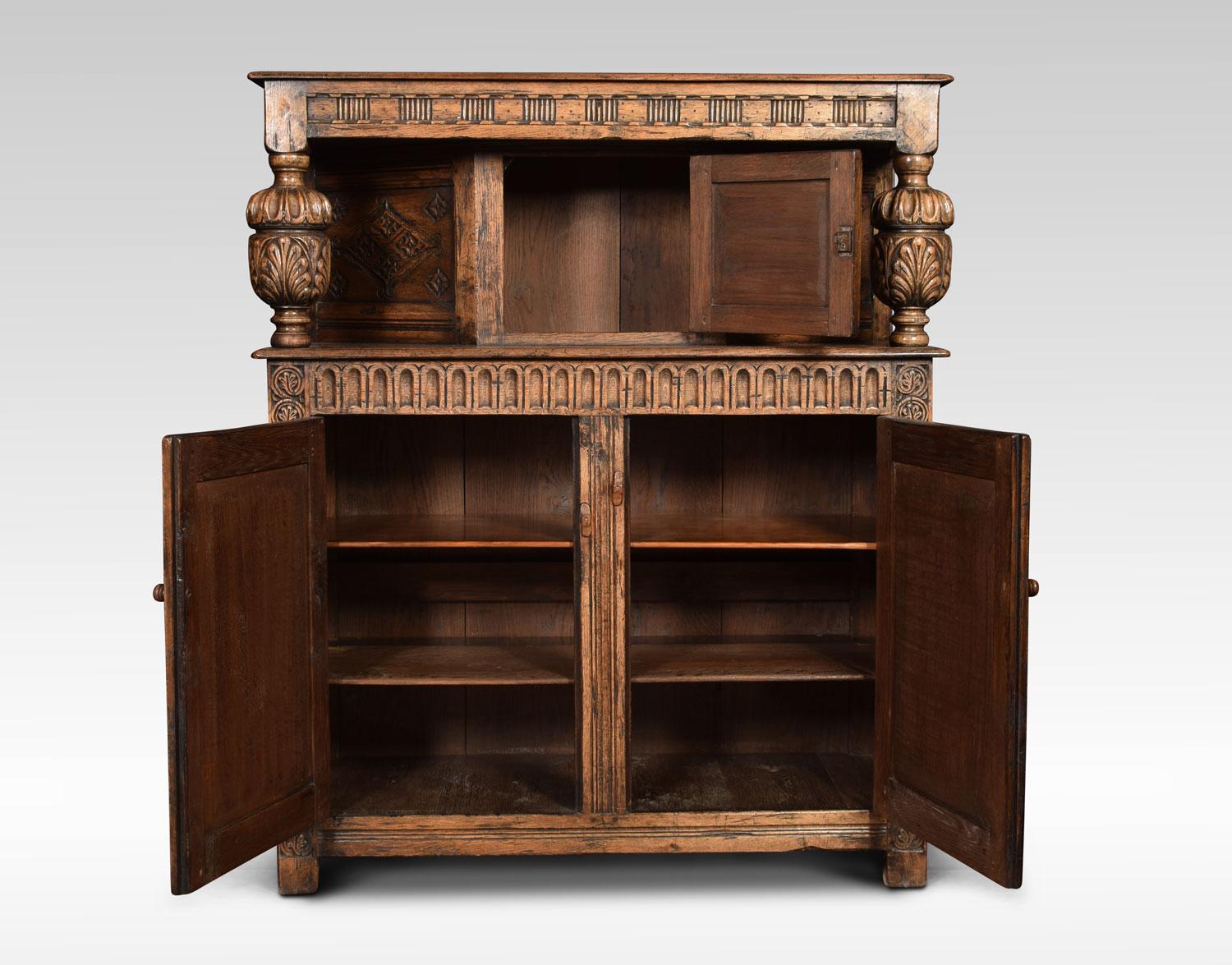 Oak court cupboard, the carved and panelled canted cupboard supported on turned cup and cover supports and arcaded frieze. The base section with two arched panelled doors opening to reveal shelved interior. Flanked by foliate carved