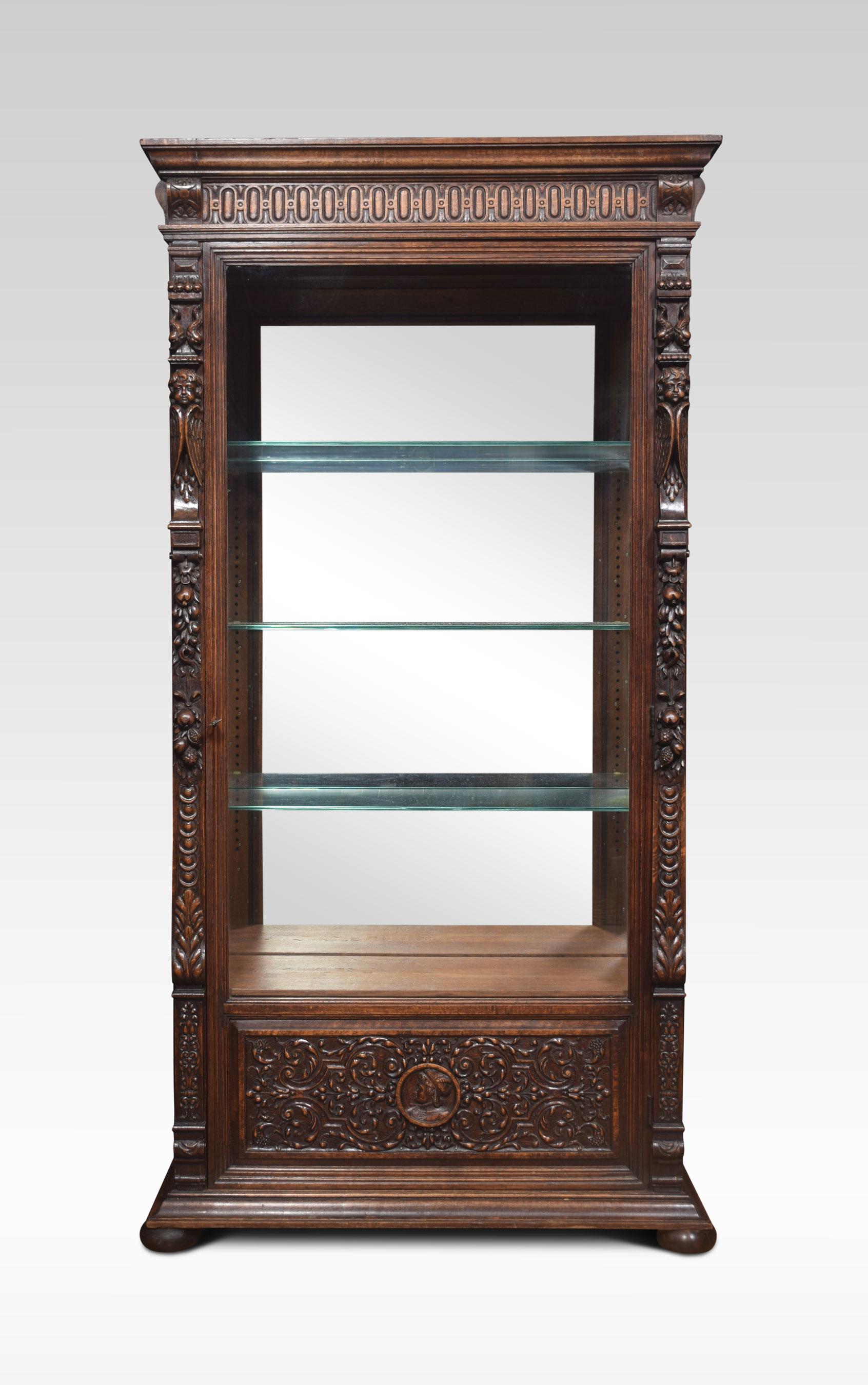 Oak display cabinet the projecting molded cornice above a large glazed door encased in carved frame with winged cherubs leaves and floral scroll relife. The door opening to reveal an adjustable shelved interior and mirrored back. All raised up on