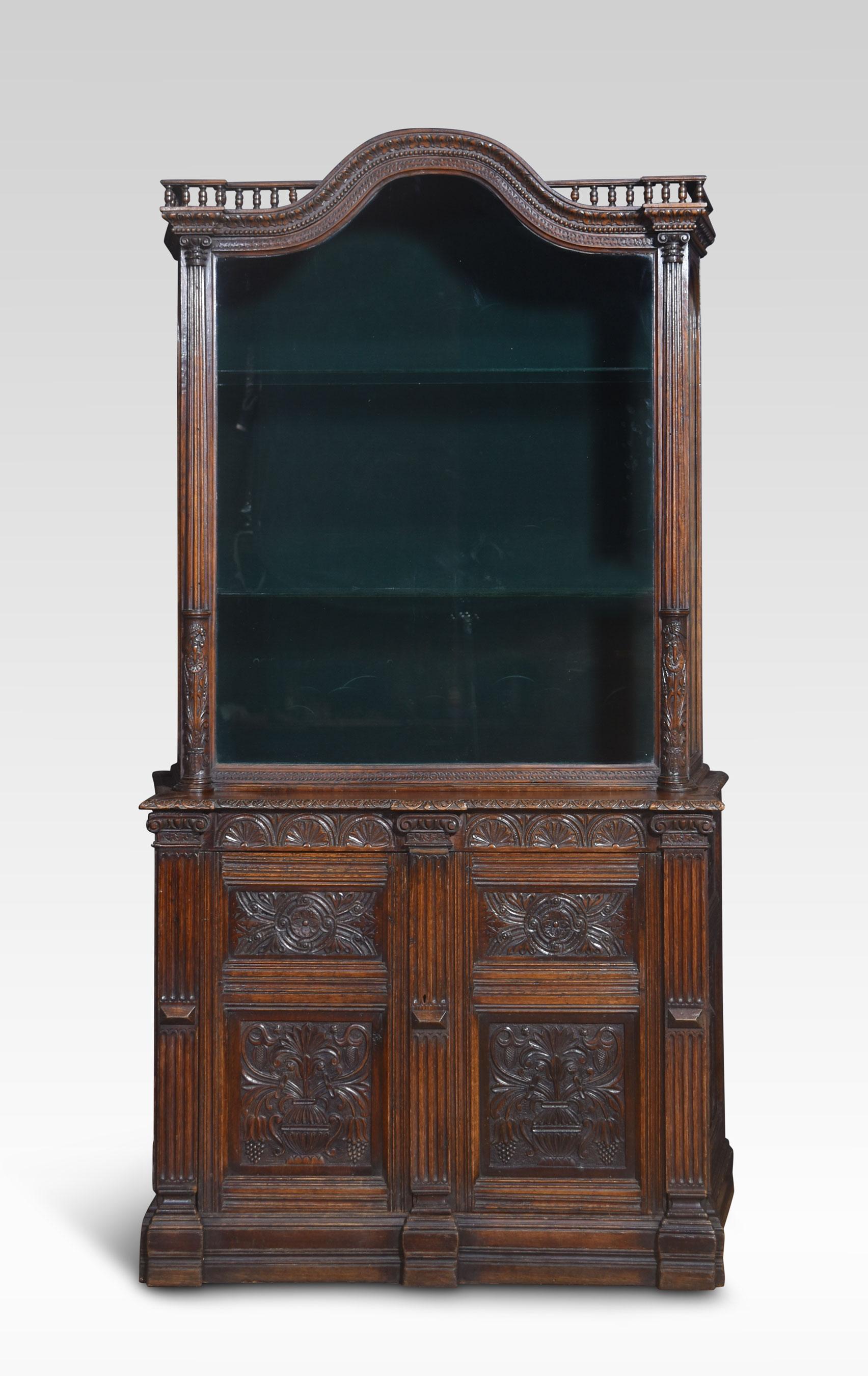 Oak display cabinet the shaped spindle top above large glazed door opening to reveal velvet lined interior and two glass shelves. To the heavily carved base section fitted with a pair of panelled doors with floral scrolling detail and reeded