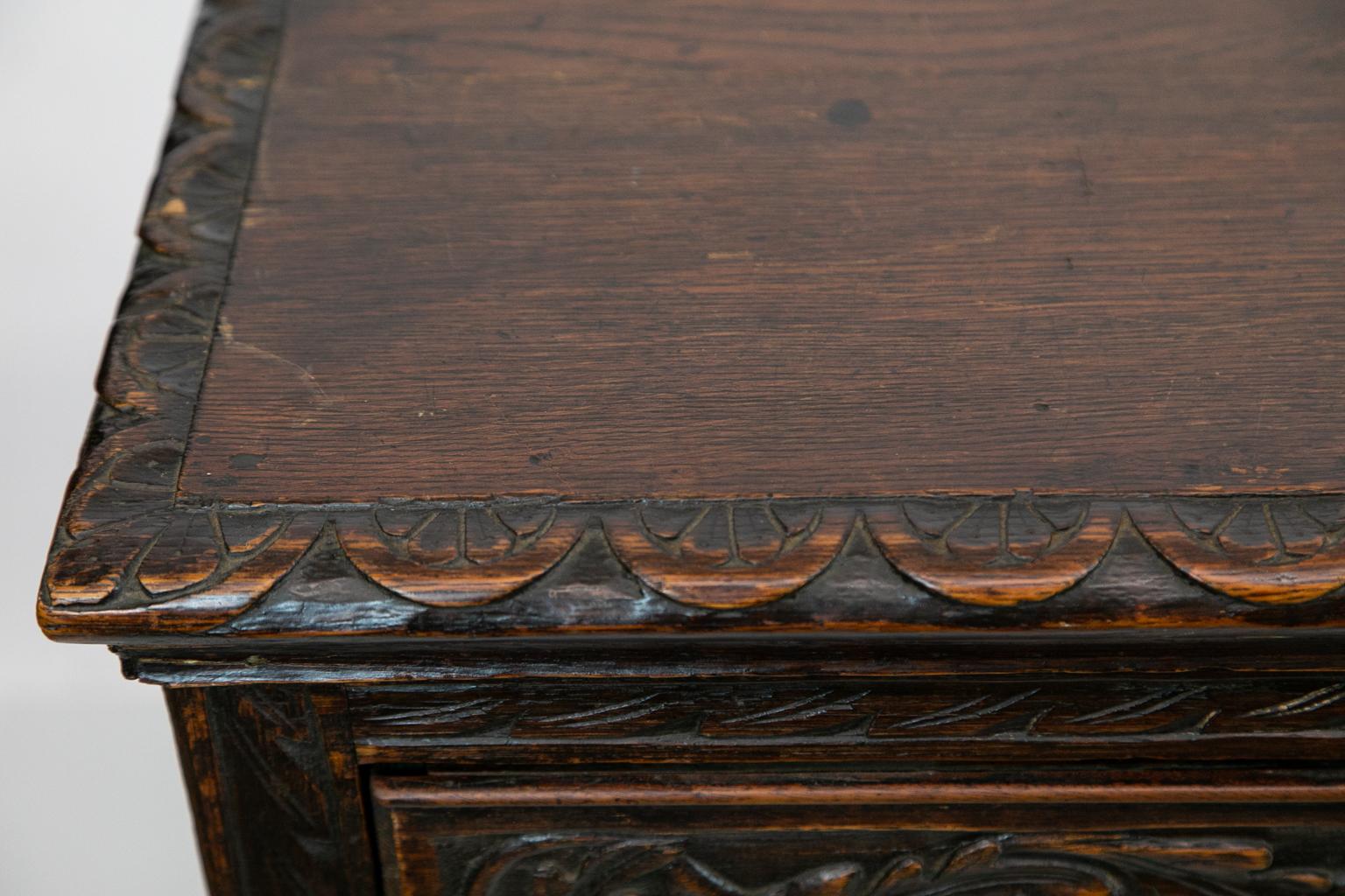 Carved oak English sideboard, with the drawers are carved with oak leaf and acorn banding and have etched brass pulls, the sides with inset panels. The apron and top moldings are carved with semicircular leaf carvings.
