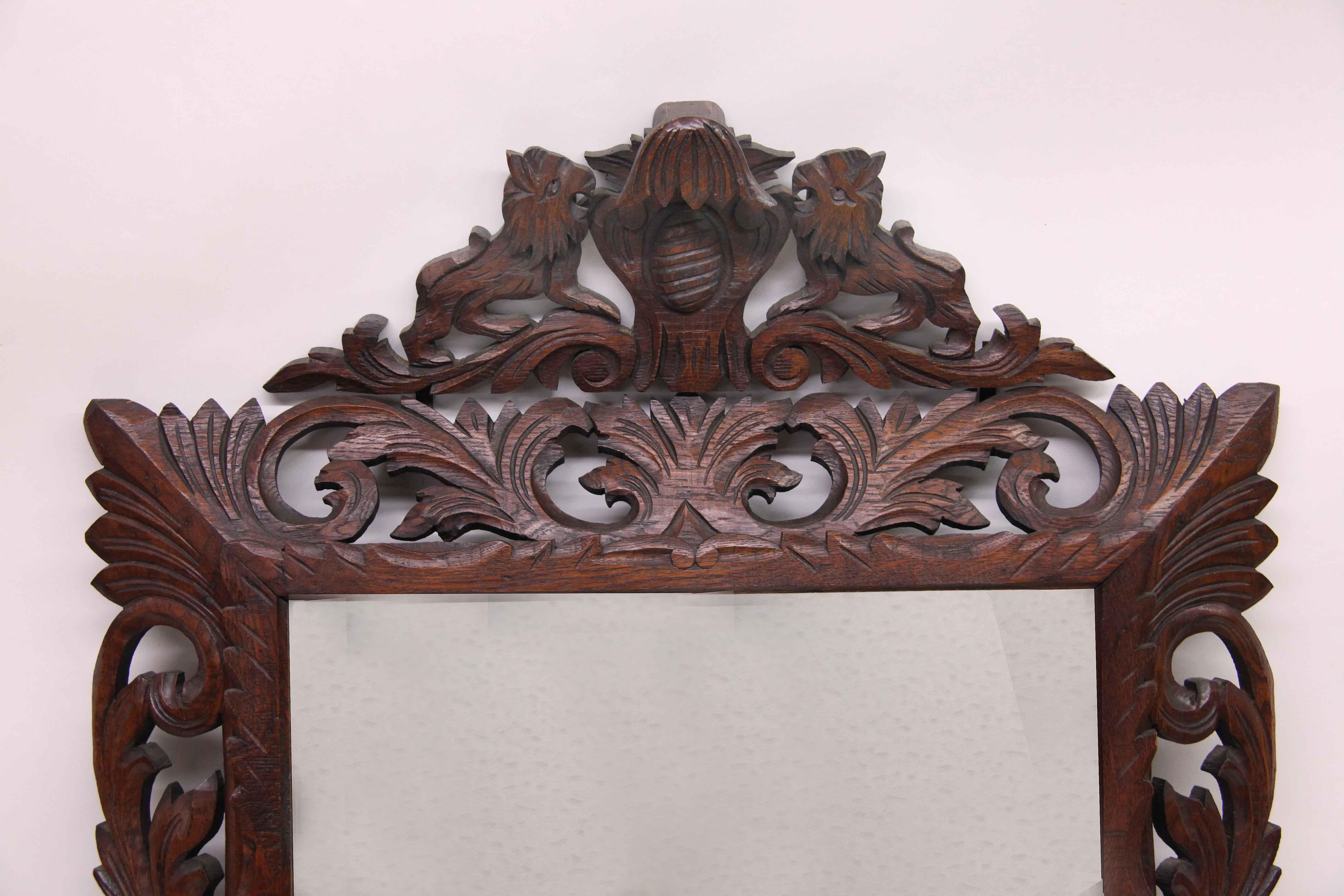 Carved oak French mirror, the separate top carving features lions facing each other between an oval vertical medallion and stylized bell flower (This piece is held on the back with metal straps). The angled carved woodwork frame has a repetitive
