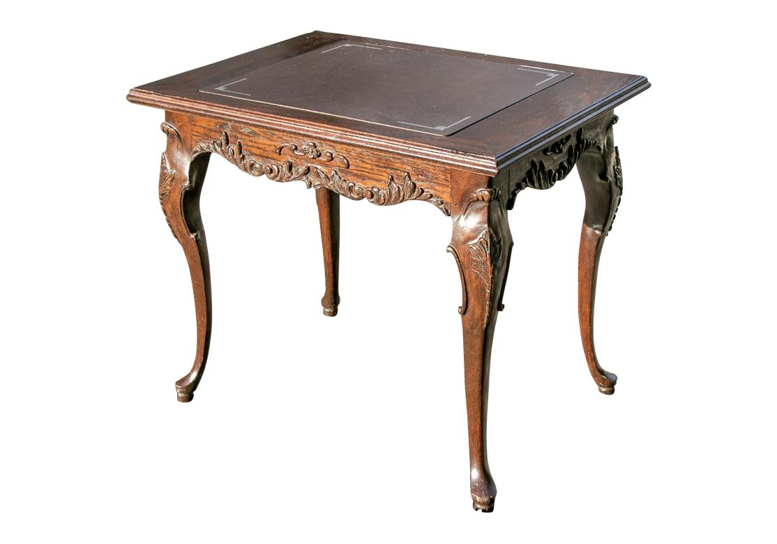 A very well made and decorative carved Oak Game Table with a reversible silver embossed leather top that lifts to reveal a colored leather inlaid Backgammon board. The table frame with some intentional distressing is carved in a Provincial French