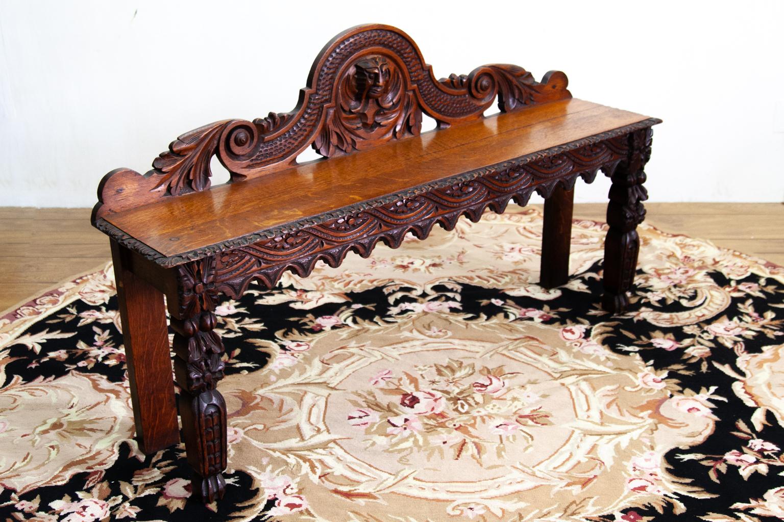 Carved oak hall bench, with center crest having a carved mask, the apron with interlaced carving and repeating pendants, intricately carved legs.