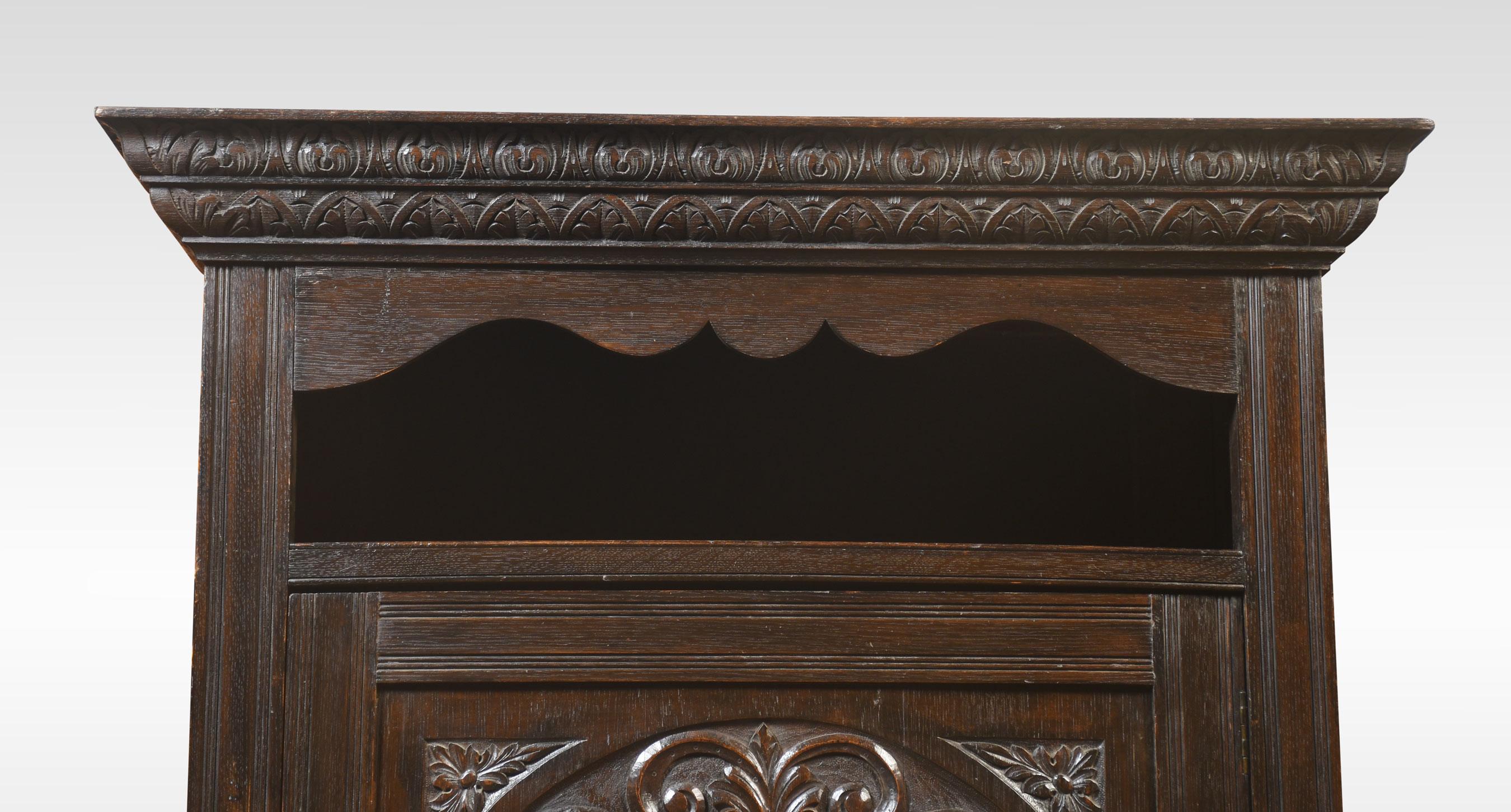 Solid oak hall robe, the moulded cornice above open cupboard to the door having urn and scrolling relief and central dolphin decoration. opening to reveal hanging area. The base is fitted with a long drawer. All raised up on a plinth